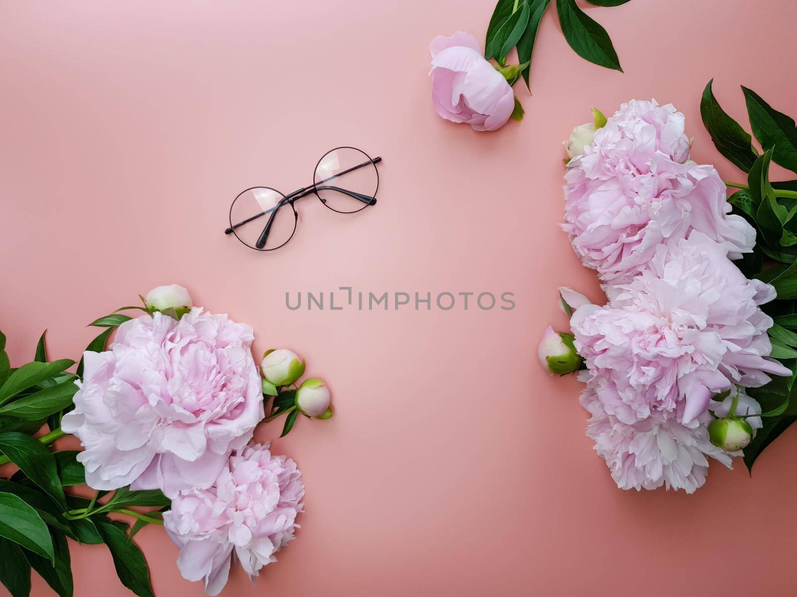 On a pink background lies a pair of glasses and pink peonies. High quality photo