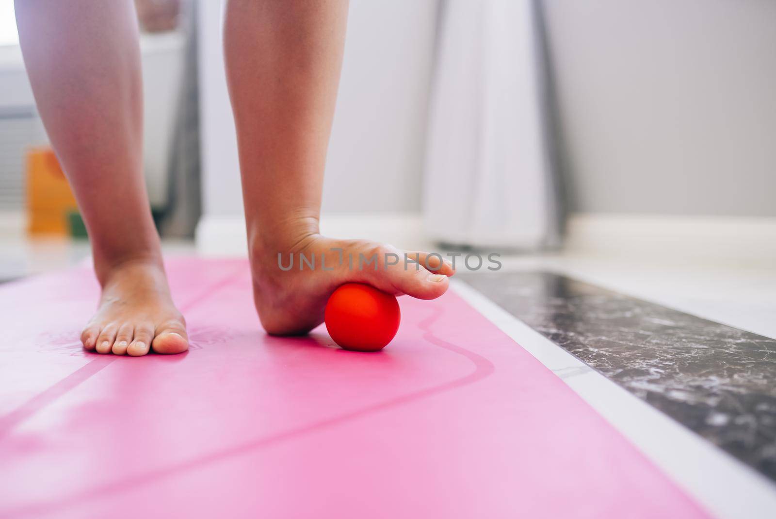 Woman massages the foot with a ball. The ball will apply pressure to the painful spot and raise the procedure