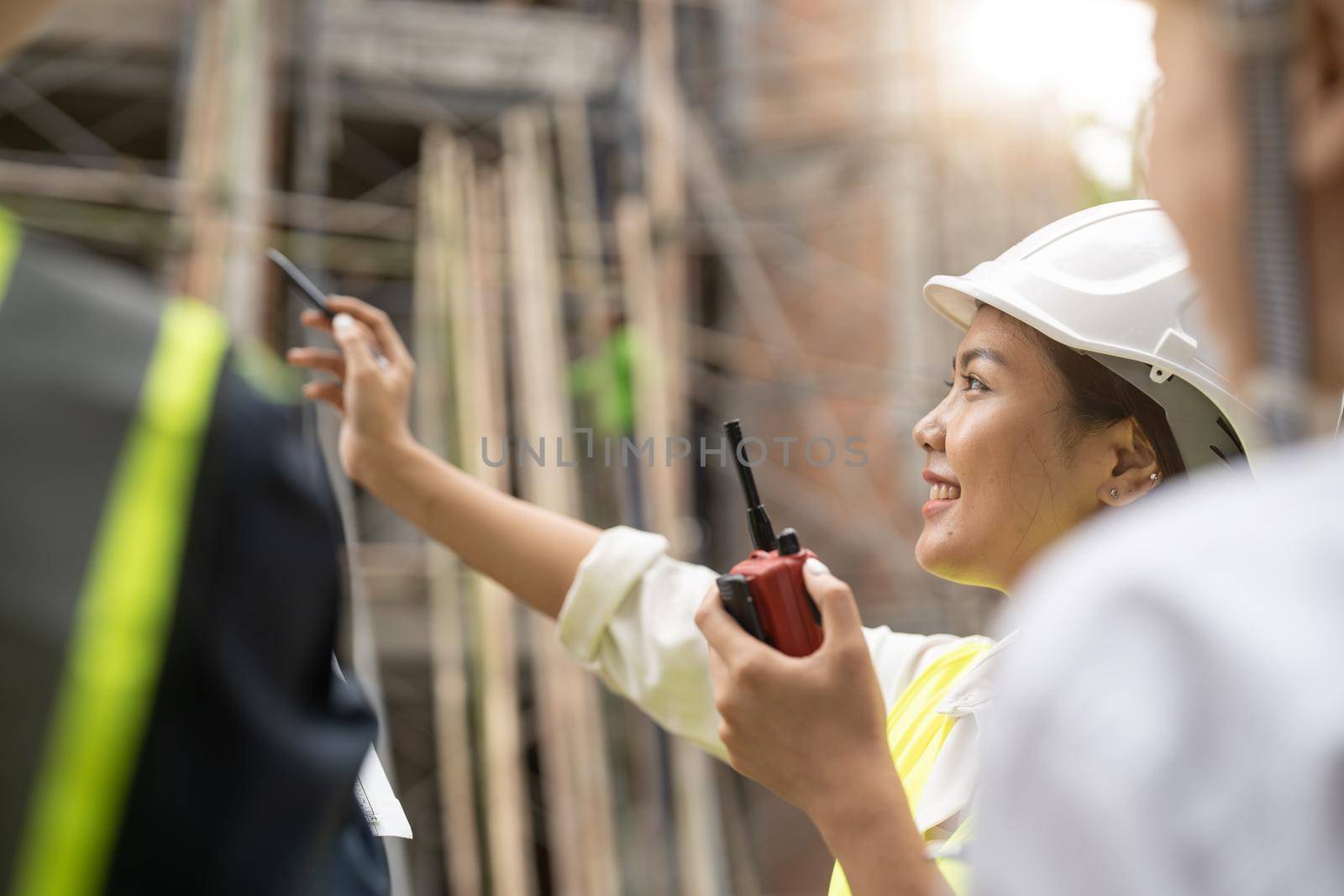 Asian female engineer using radio ordering work at construction project site.