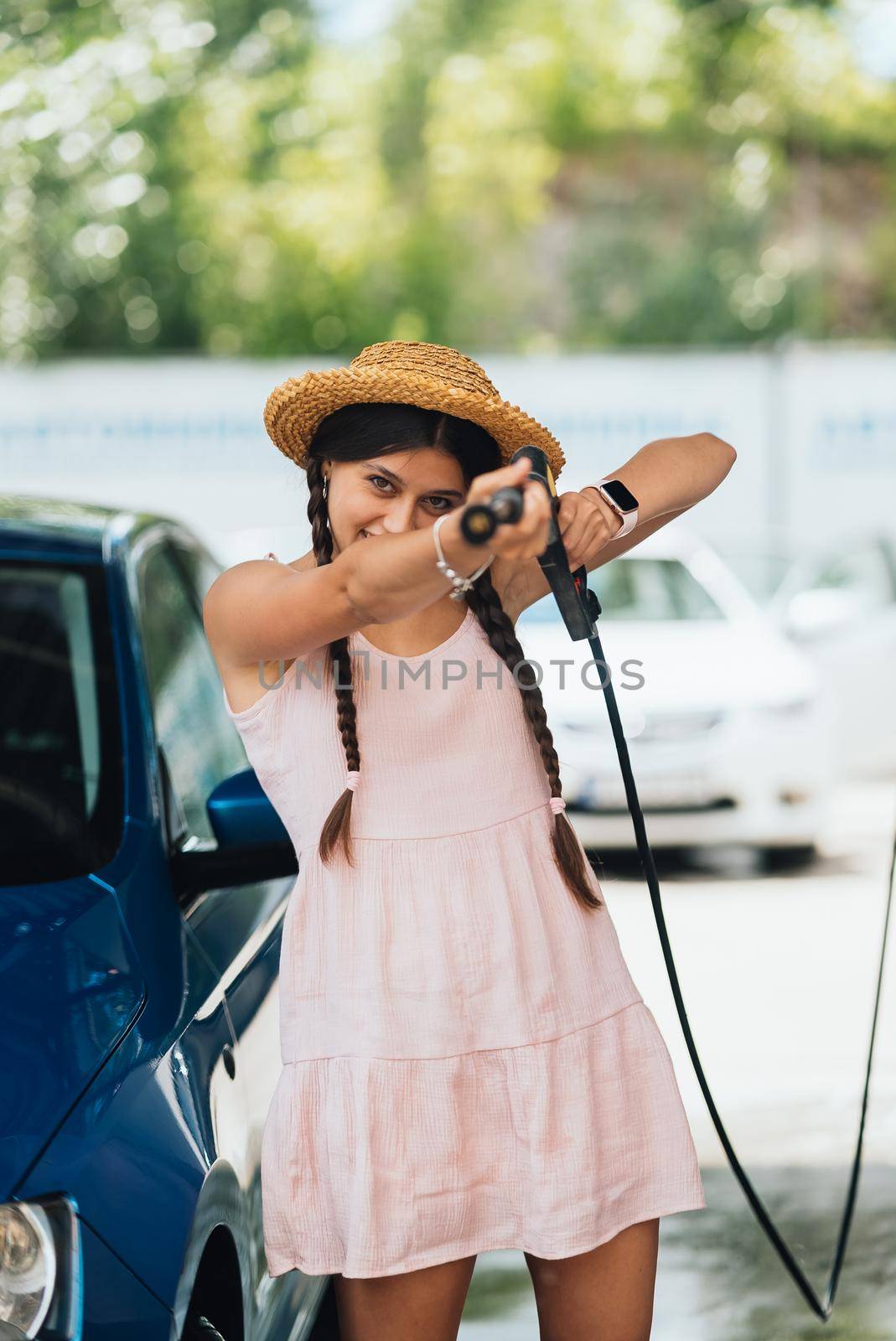 Woman with high pressure hose stands by car