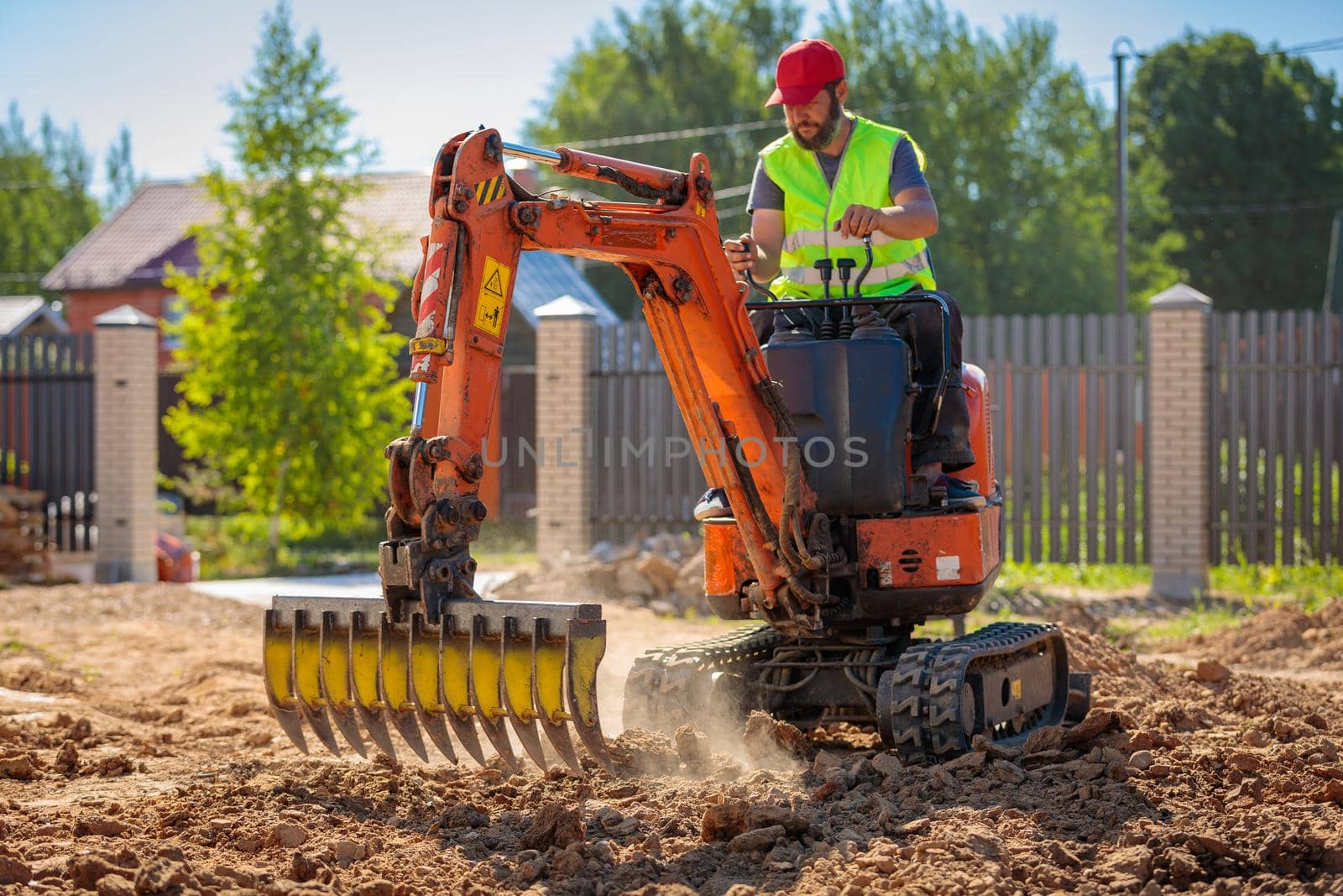 A man on a mini-excavator levels a piece of land, loosens the soil