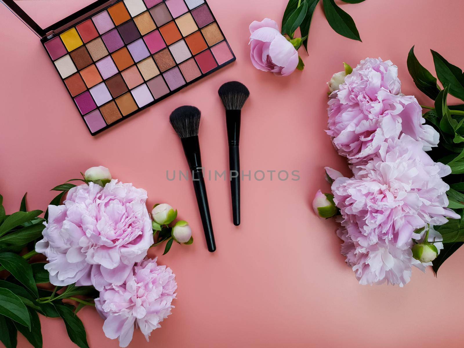 On a pink background are shadows, makeup brushes and pink peonies. High quality photo