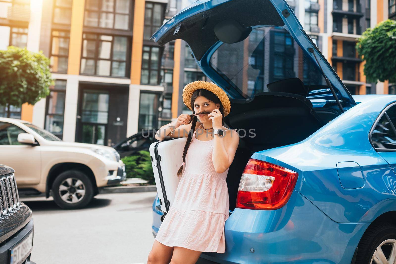 Young happy woman packing her suitcase into luggage boot of the car. Holidays concept.