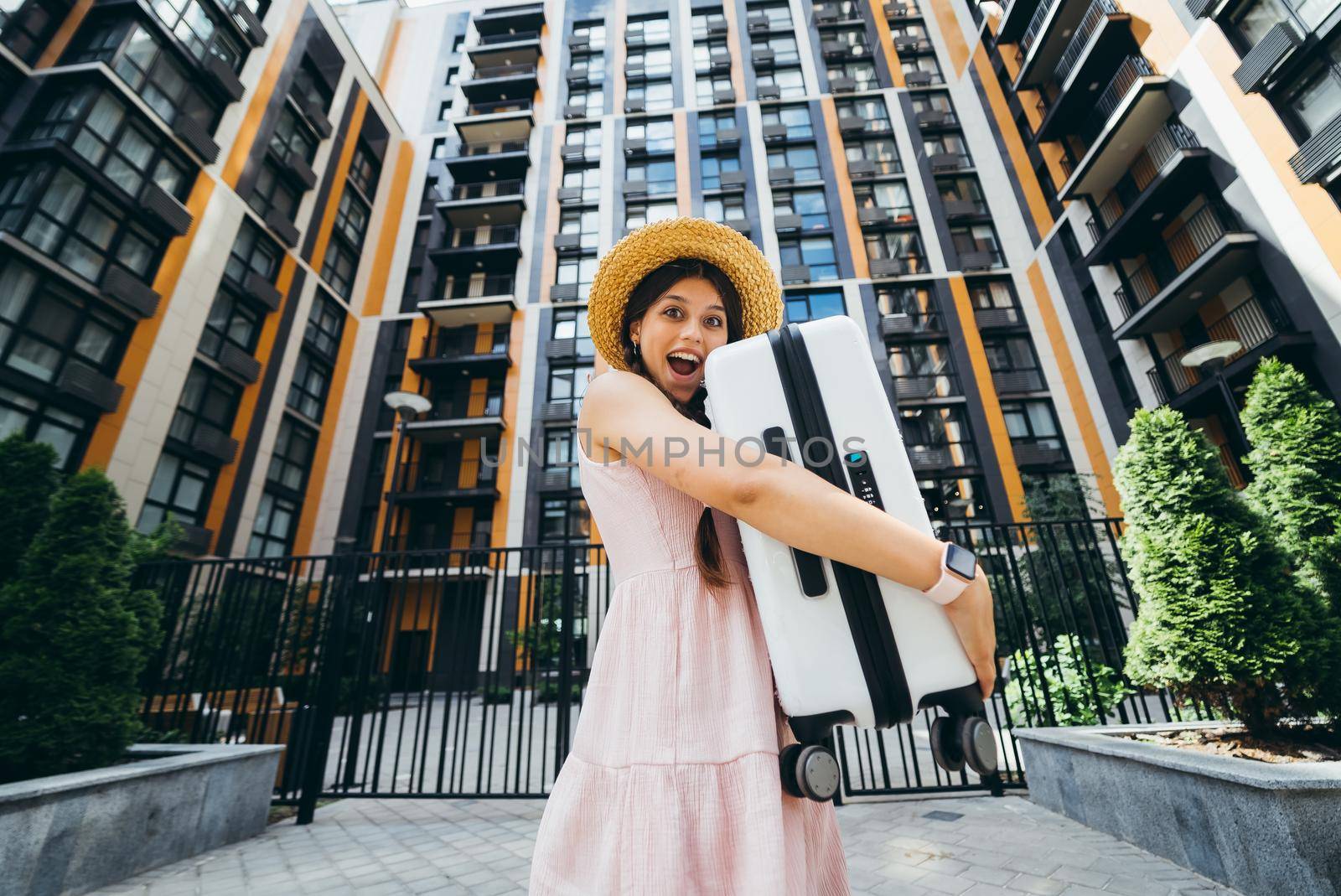 A young beautiful woman holds a suitcase in her hands in front of a modern house