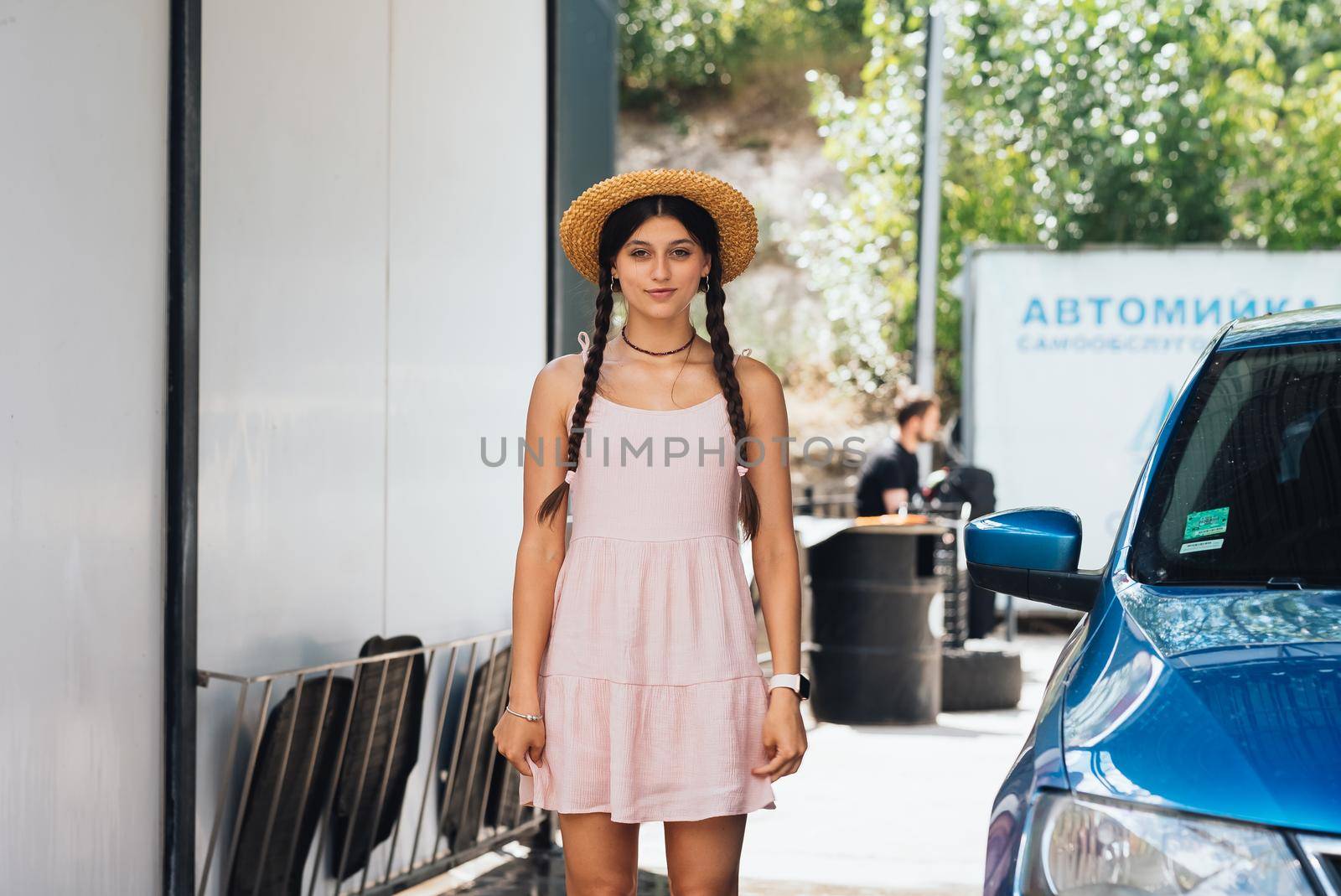 Beautiful young woman in a short dress with tails and a hat at the car wash