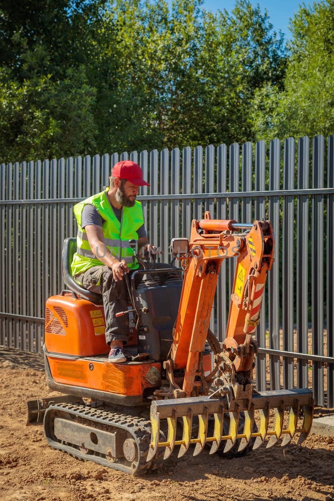 A man on a mini-excavator levels a piece of land, loosens the soil