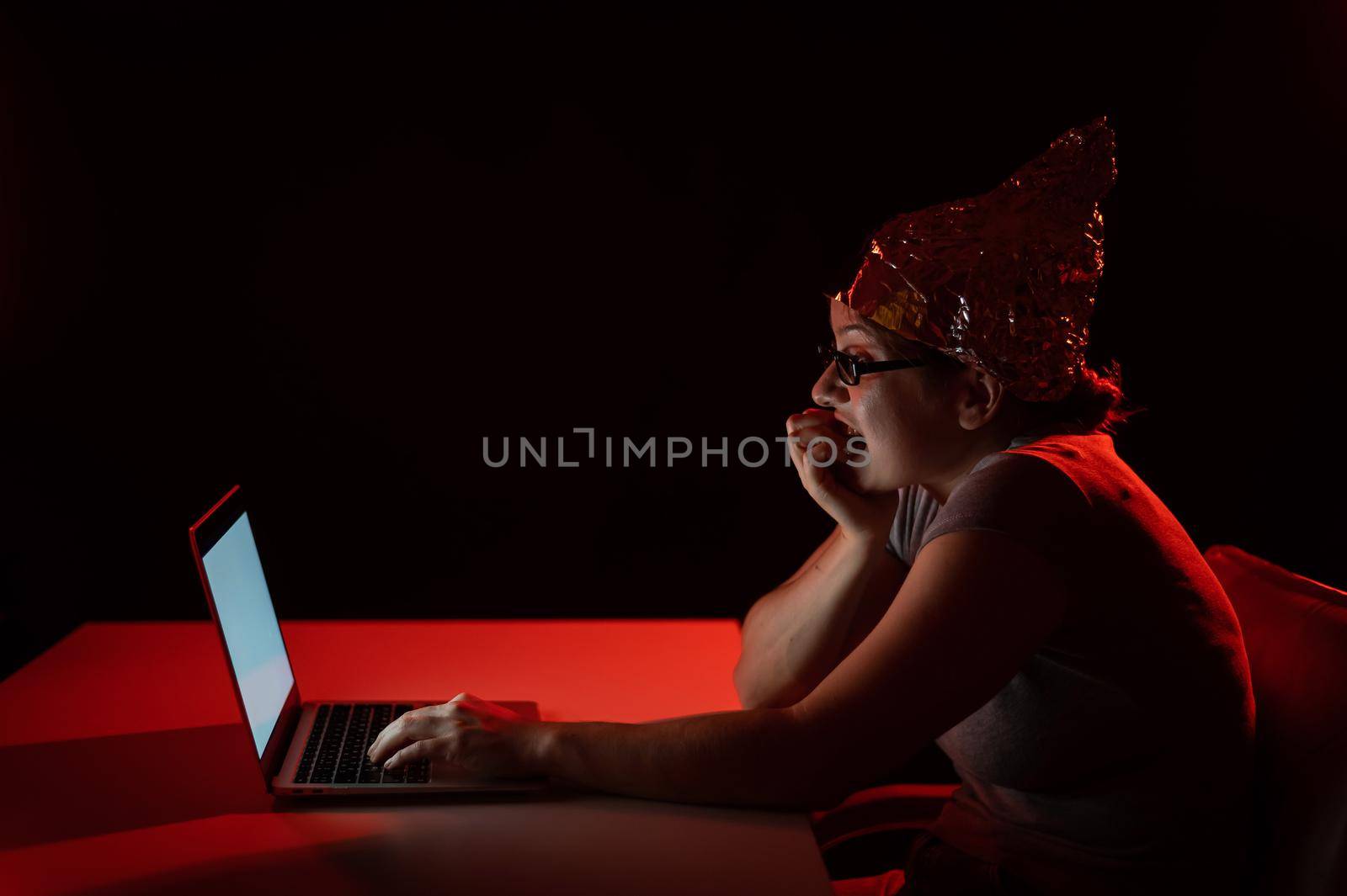 Paranoid caucasian woman typing on a computer wearing a tinfoil cap. Conspiracy theory