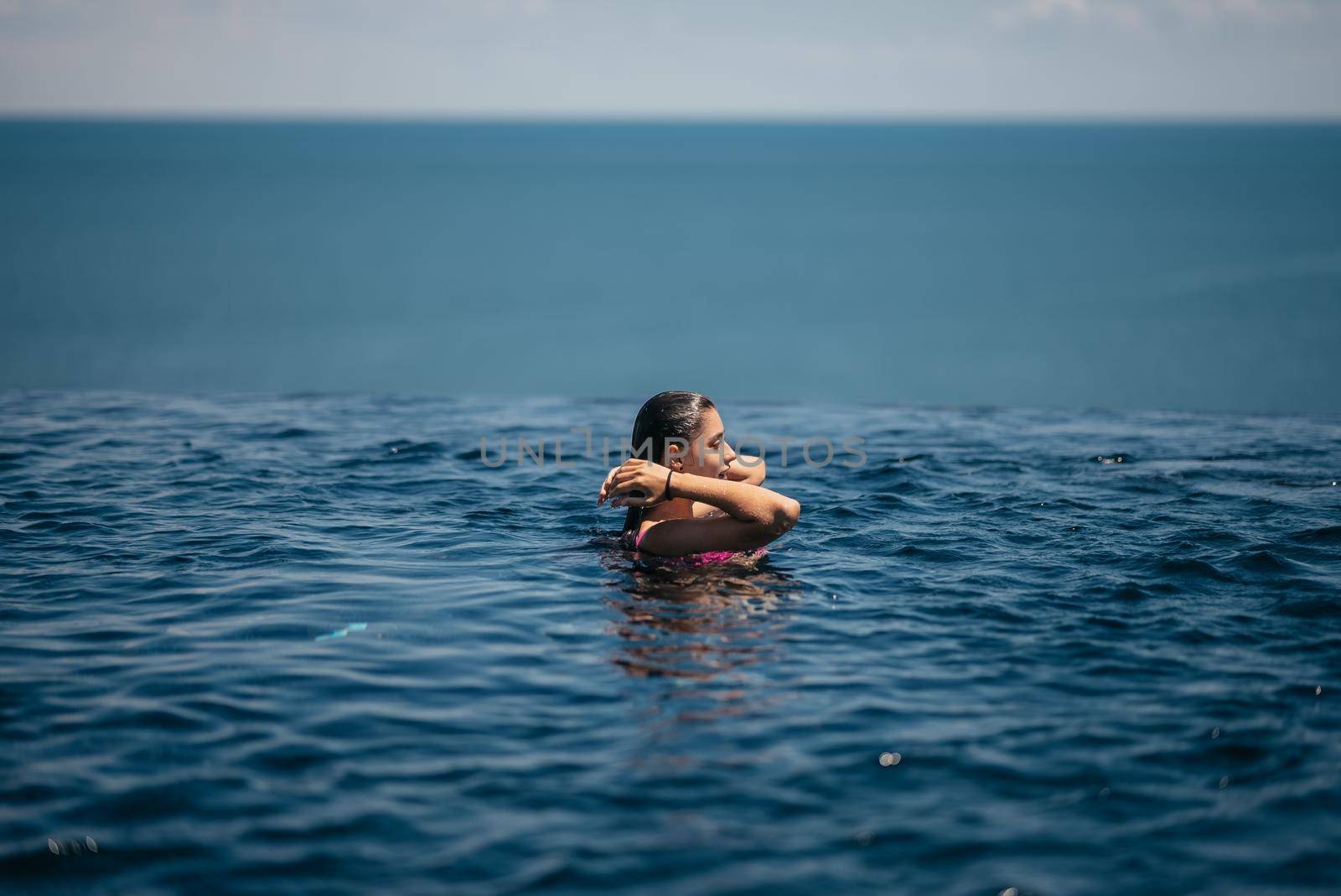 Happy woman in swimsuit swimming in infinity pool at luxury hotel against seafront. Relaxing, summer, travel, holiday, vacation and weekend concept