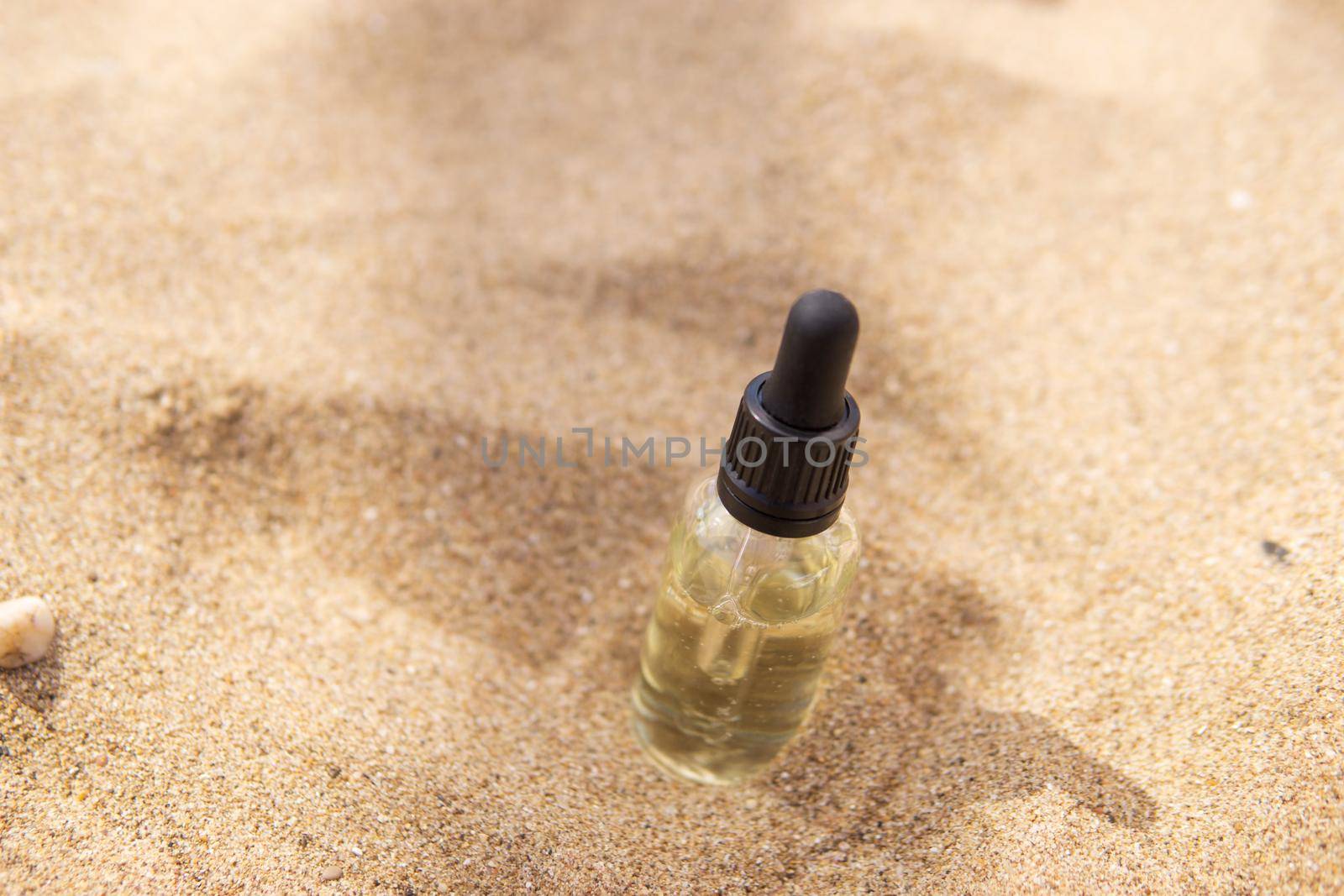 Cosmetic serum for the skin in a glass bottle. A bottle with a pipette on a sandy beach by the sea. Essences for skin care on a sandy background. The concept of natural cosmetics and SPA products.