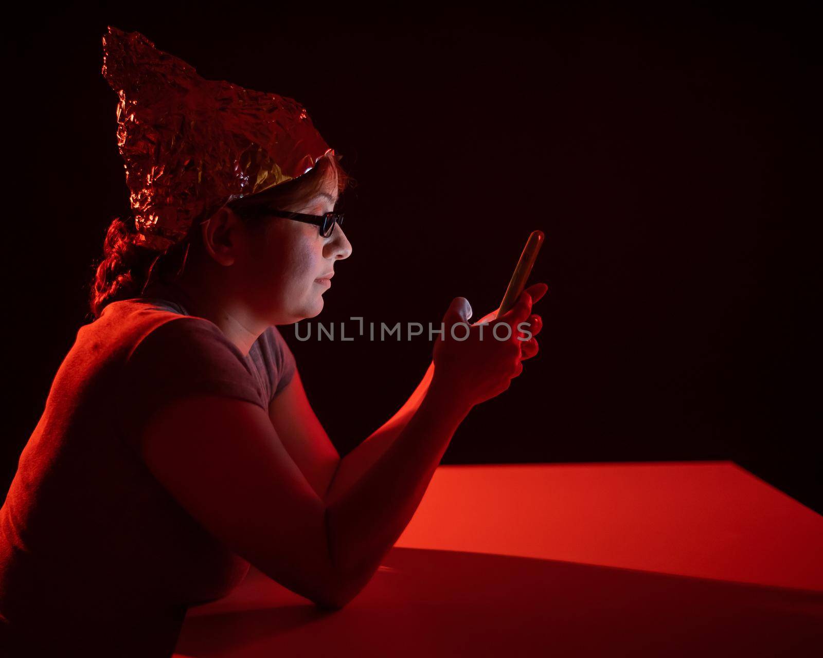 Paranoid caucasian woman using smartphone wearing tinfoil hat. Conspiracy theory