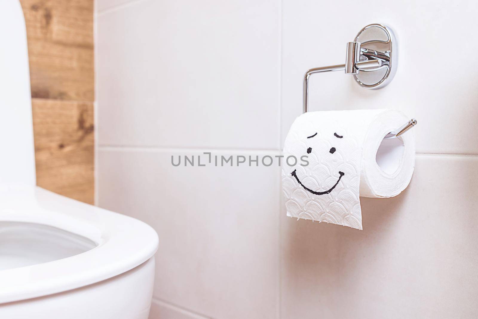 Close-up of a toilet paper roll with a funny smiley face hanging on the wall in the bathroom. The concept of good health, clean bathroom, happy life