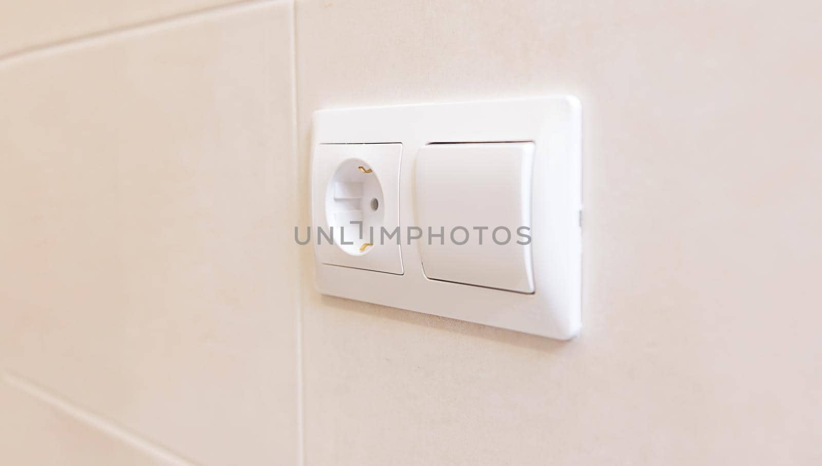 close-up of an electric socket and a light switch on a white ceramic tile wall. White copy paste space for your design. Modern European interior