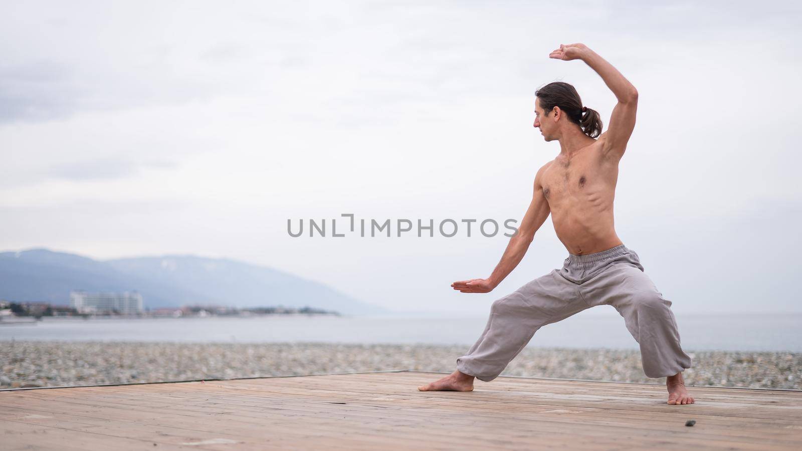 Caucasian man with naked torso practicing wushu on the seashore