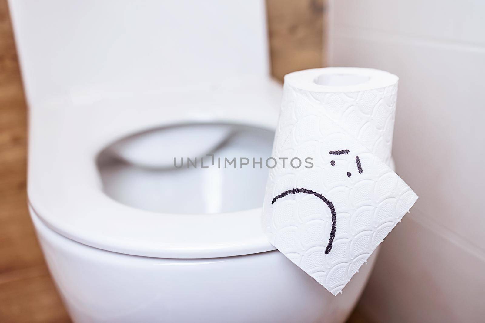 A close-up of a toilet paper roll with a funny emoji stands on a toilet bowl with an open lid in the bathroom. The concept of good health, clean bathroom, happy life
