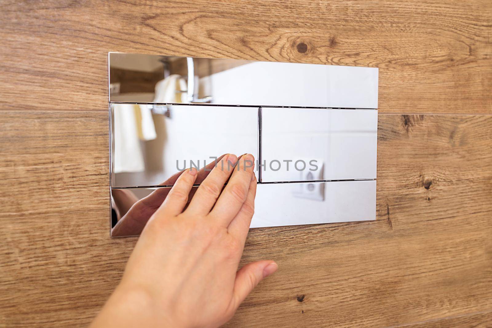 close-up, a woman's hand presses the flush button to the toilet. Plumbing equipment hanging on a wooden wall. Modern design, bathroom interior, simple, stylish solutions