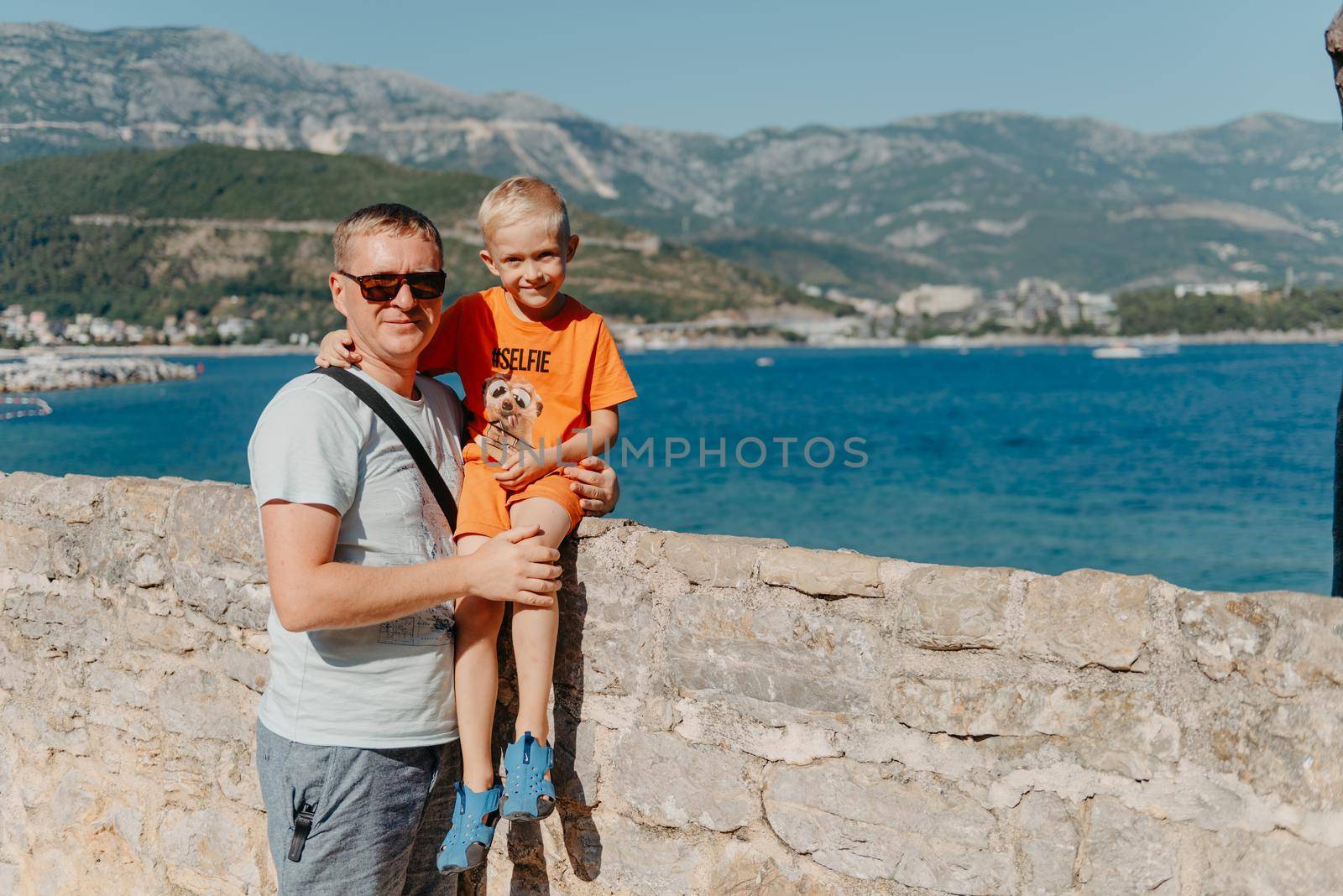 Cute family are having fun on the beach. Father and child against the background of the blue sea and sky. Travel, active lifestyle, vacation, rest concept. a man with a child on the shore. tourists on the shore of Budva, Montenegro by Andrii_Ko