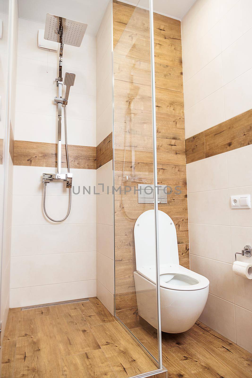 Minimalistic modern bathroom interior, close-up. Glass shower cubicle, chrome accessories and shower, and white, clean toilet. White and wooden ceramic tiles on the walls and on the floor