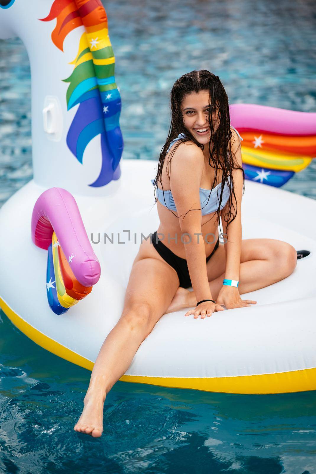 Woman in bikini in inflatable unicorn toy mattress float in pool. Girl relaxing sunbathing enjoying travel holidays at resort pool