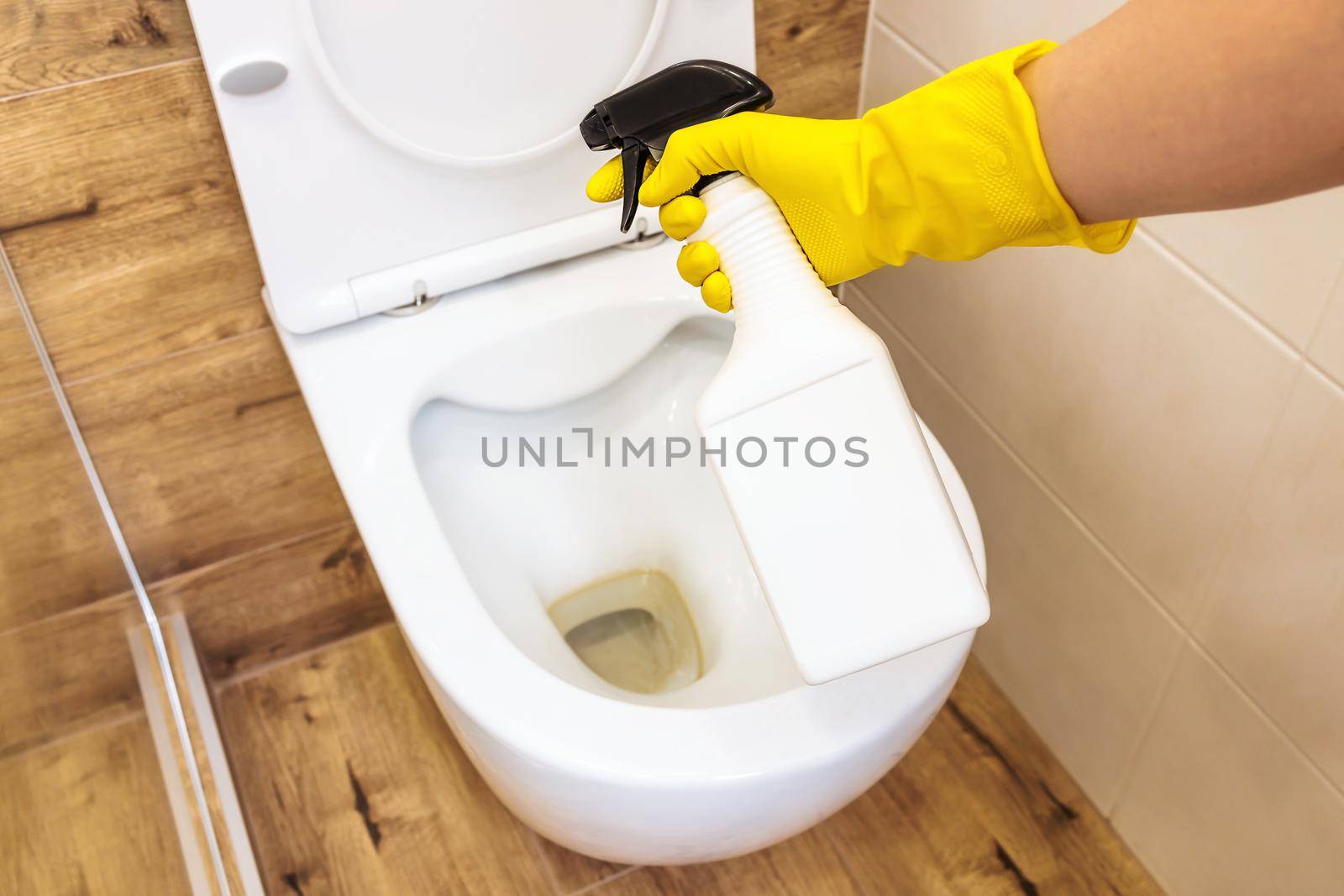 Mockup of plastic white bottle with toilet cleaner, place for logo. Close-up of female hands in yellow protective gloves using detergent solution for toilet cleaning, disinfection and hygiene concept