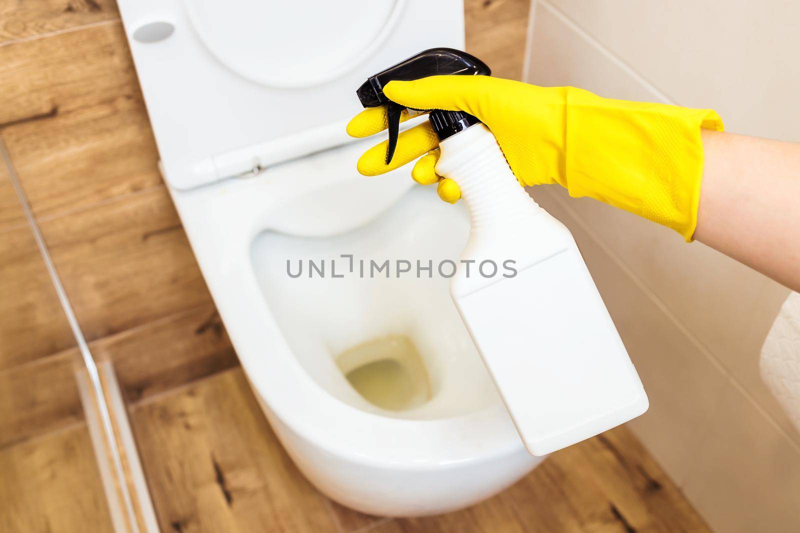 Mockup of plastic white bottle with toilet cleaner, place for logo. Close-up of female hands in yellow protective gloves using detergent solution for toilet cleaning, disinfection and hygiene concept
