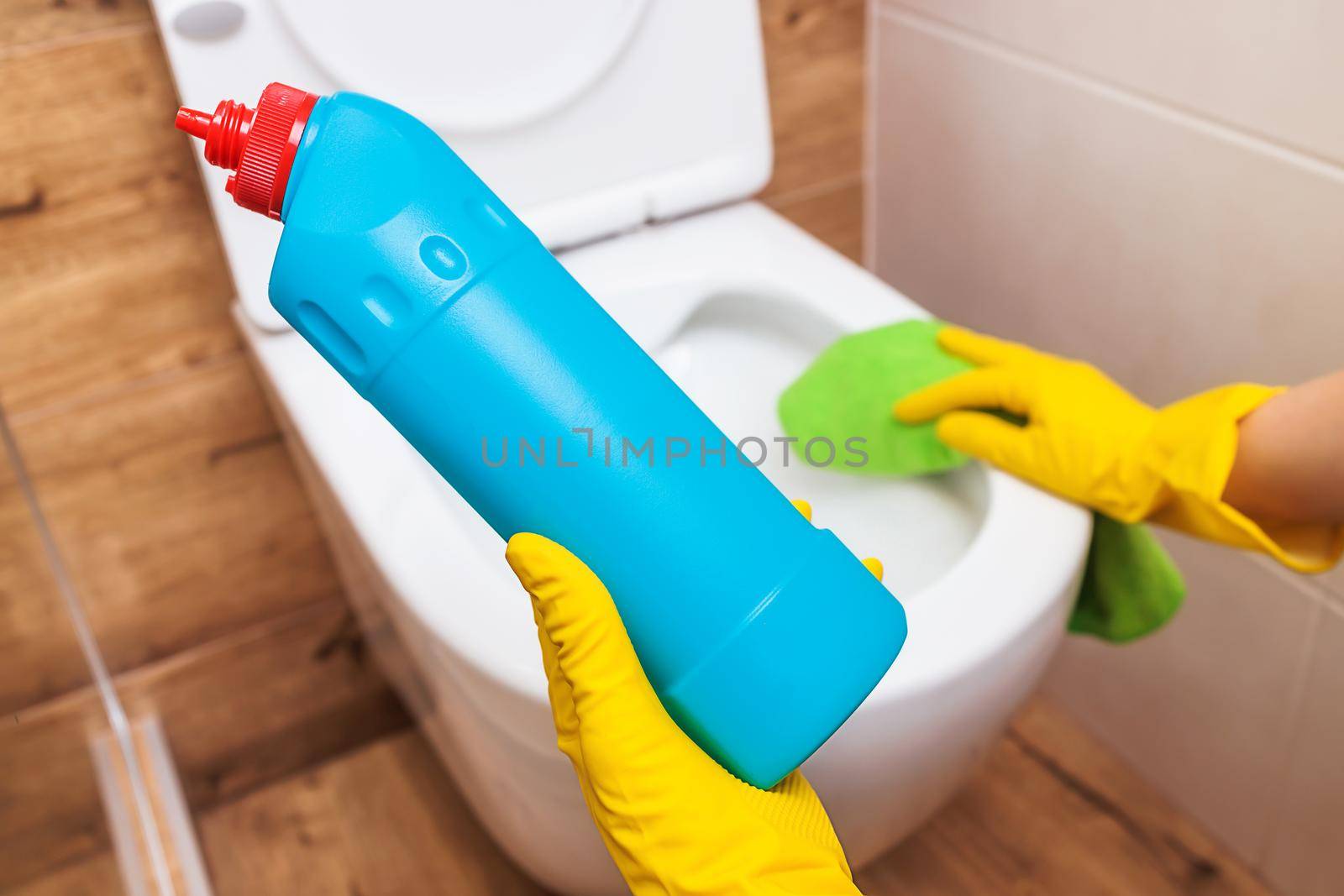 close-up, female hands in protective yellow gloves with liquid detergent to disinfect the toilet and bathroom. Mockup of a blue cleaning bottle. The concept of hygiene, house cleaning or public place
