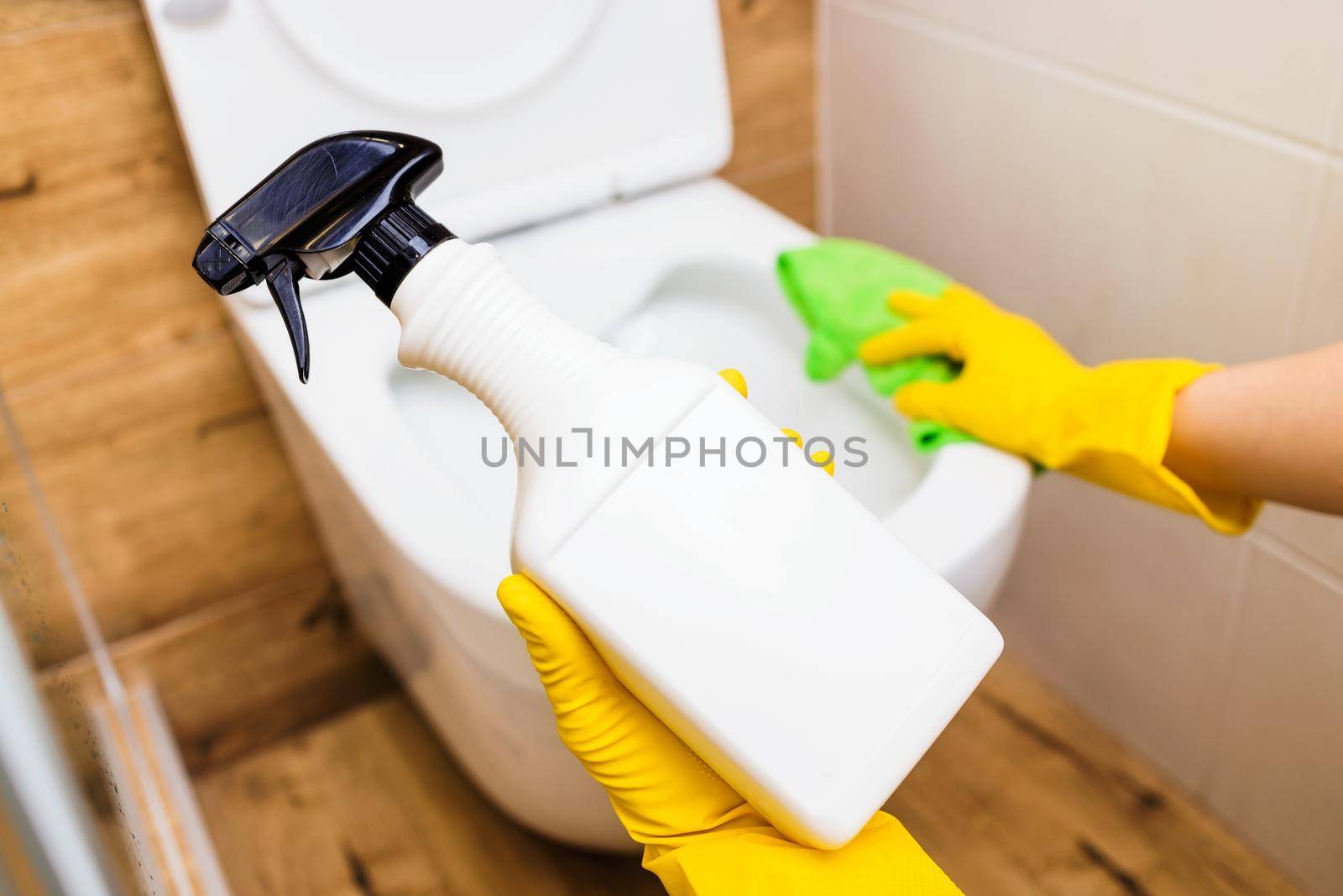 Mockup of a plastic white bottle with toilet cleaner, space for a logo. Close-up of female hands in protective gloves using cleaning solution and rags for cleaning, disinfection and toilet hygiene
