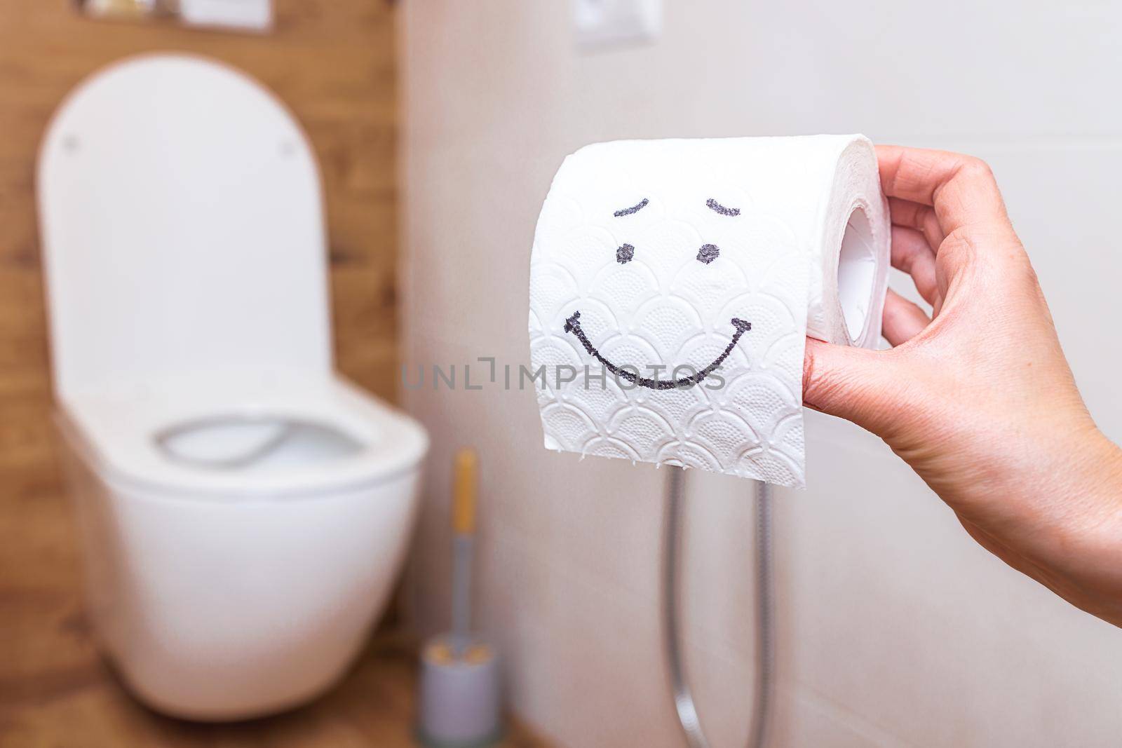 close-up, in a woman's hand a roll of toilet paper with a painted happy face. Copy space for health, medicine and personal care. Against the backdrop of a dressing room in a modern style