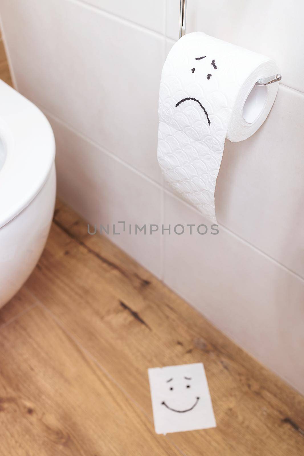 close-up, a roll of toilet paper with a painted sad face hanging on the wall. On the floor is a torn piece of paper with a cheerful face. The concept of ill health, stomach problems, copy paste