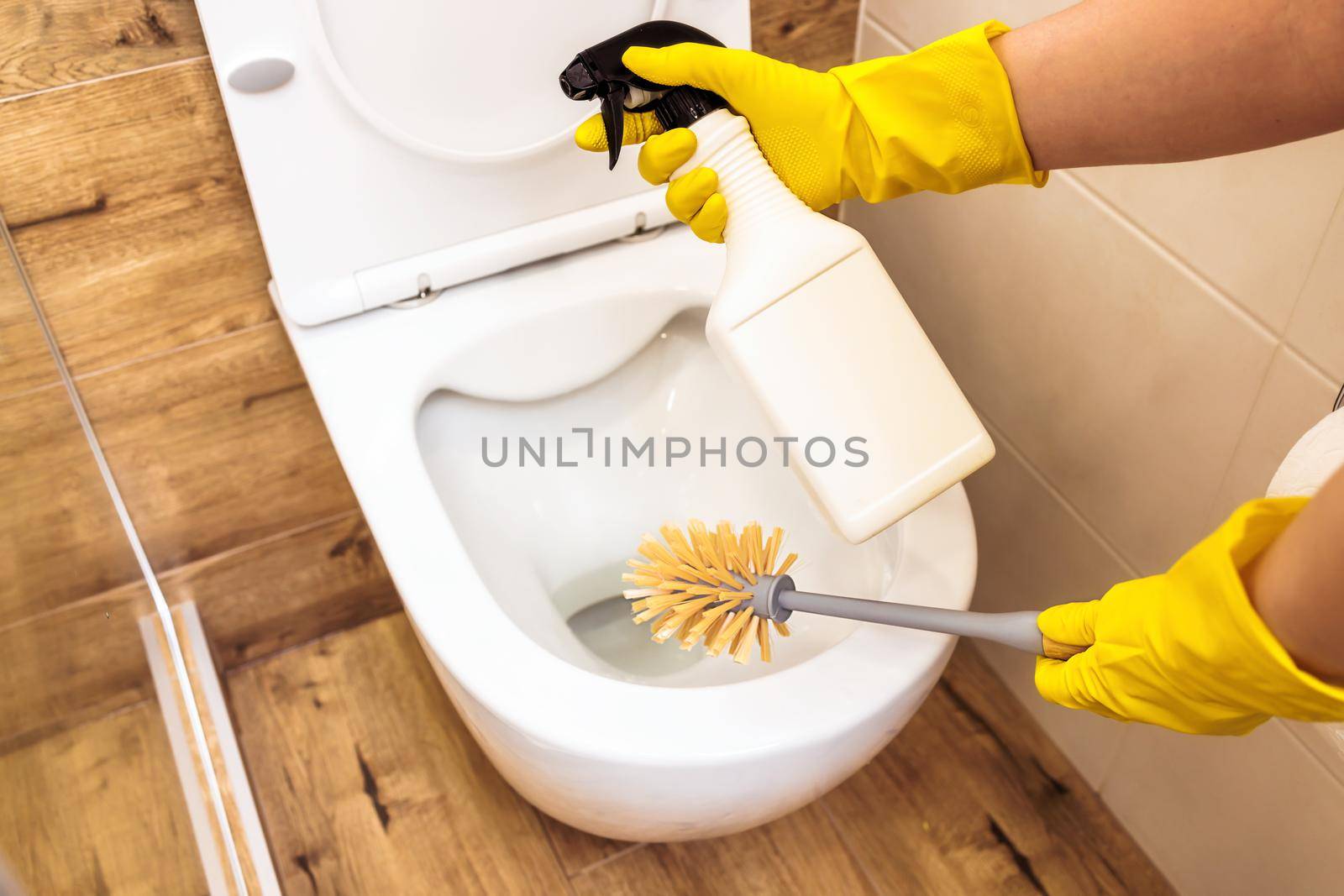 Close-up of hands using brush and cleaning solution to disinfect toilet, bottle mockup by Ramanouskaya