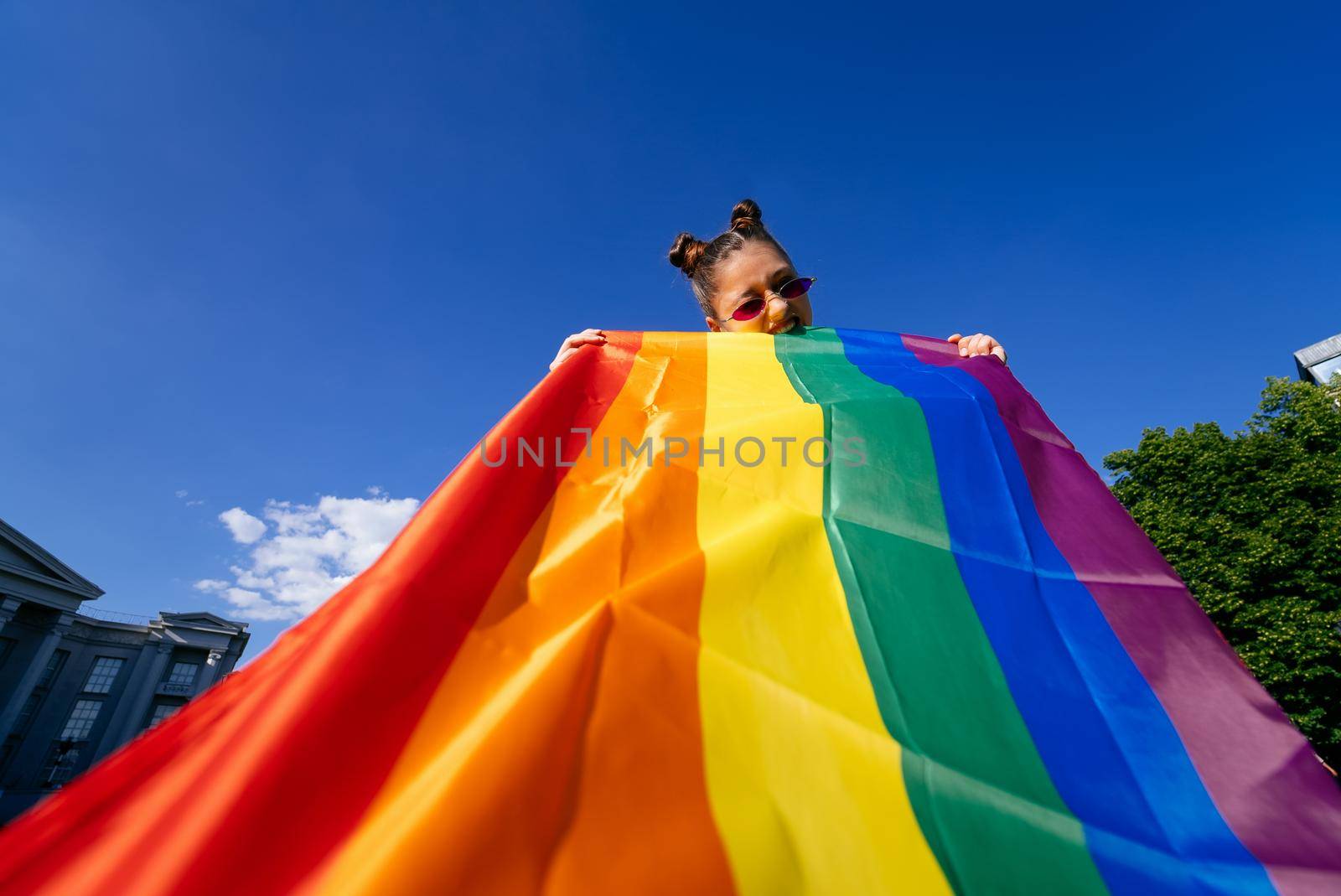 A young woman develops a rainbow flag against the sky in support of the LGBT community