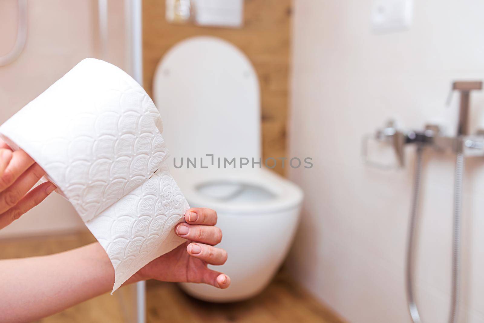 Bathroom background, closeup of woman's hand holding roll of white toilet paper, copy paste space. The concept of hygiene, cleanliness, human health and the importance of gentle personal care products