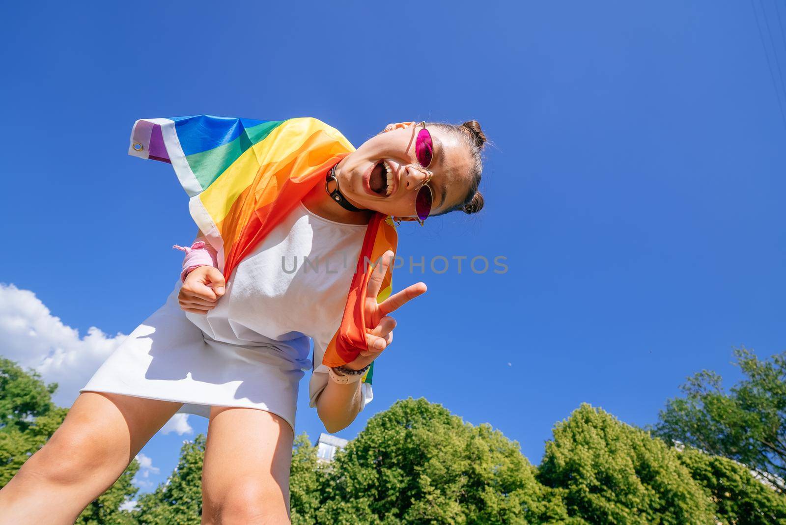 A young woman develops a rainbow flag against the sky in support of the LGBT community
