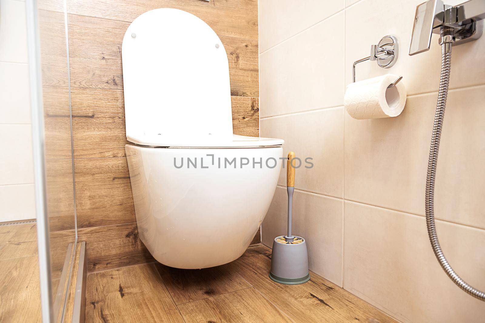 Small bathroom interior. Close-up of plumbing. white toilet bowl and hygienic bidet shower in the bathroom with ceramic tiles in natural wood-like colors and white, in a Scandinavian style.