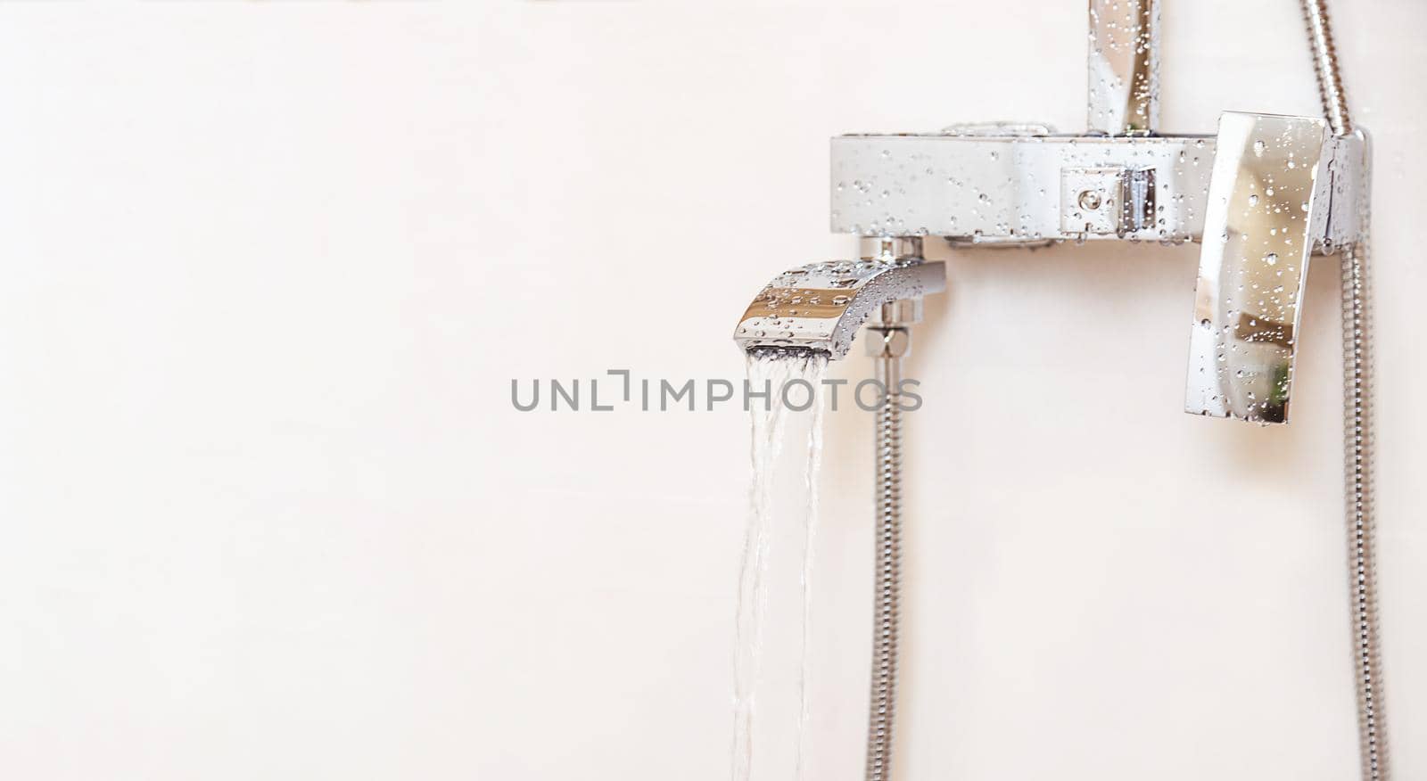 Close-up, plumbing equipment. Chrome plated water faucet hangs from the heart on a white wall, isolated object, copy space. Water flows from the faucet in a strong stream.