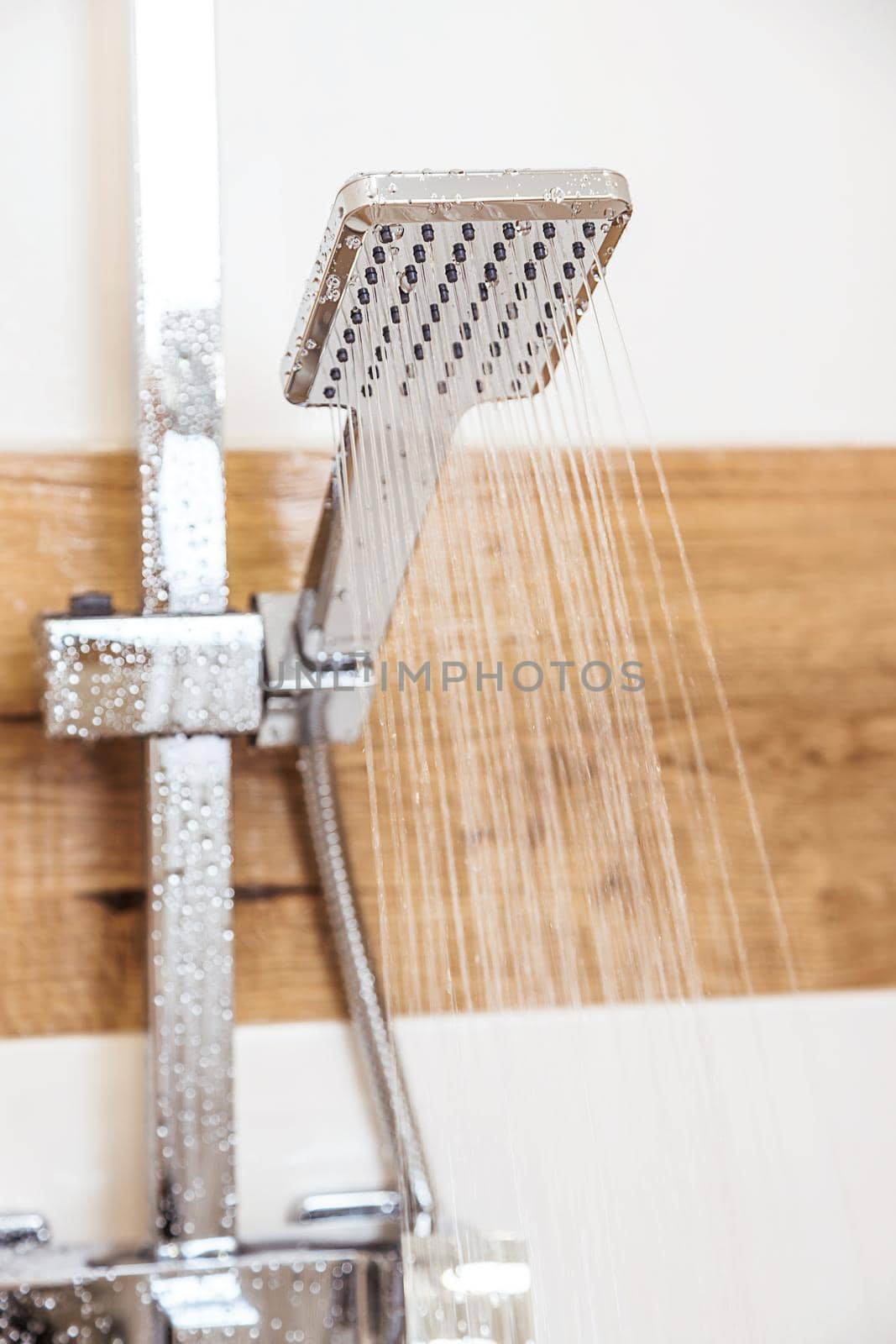 Close-up of a chrome shower, plumbing fixtures, hanging on the wall of a modern bathroom. Pure water flows from it. The concept of personal hygiene, health. Renewable resource, reasonable consumption