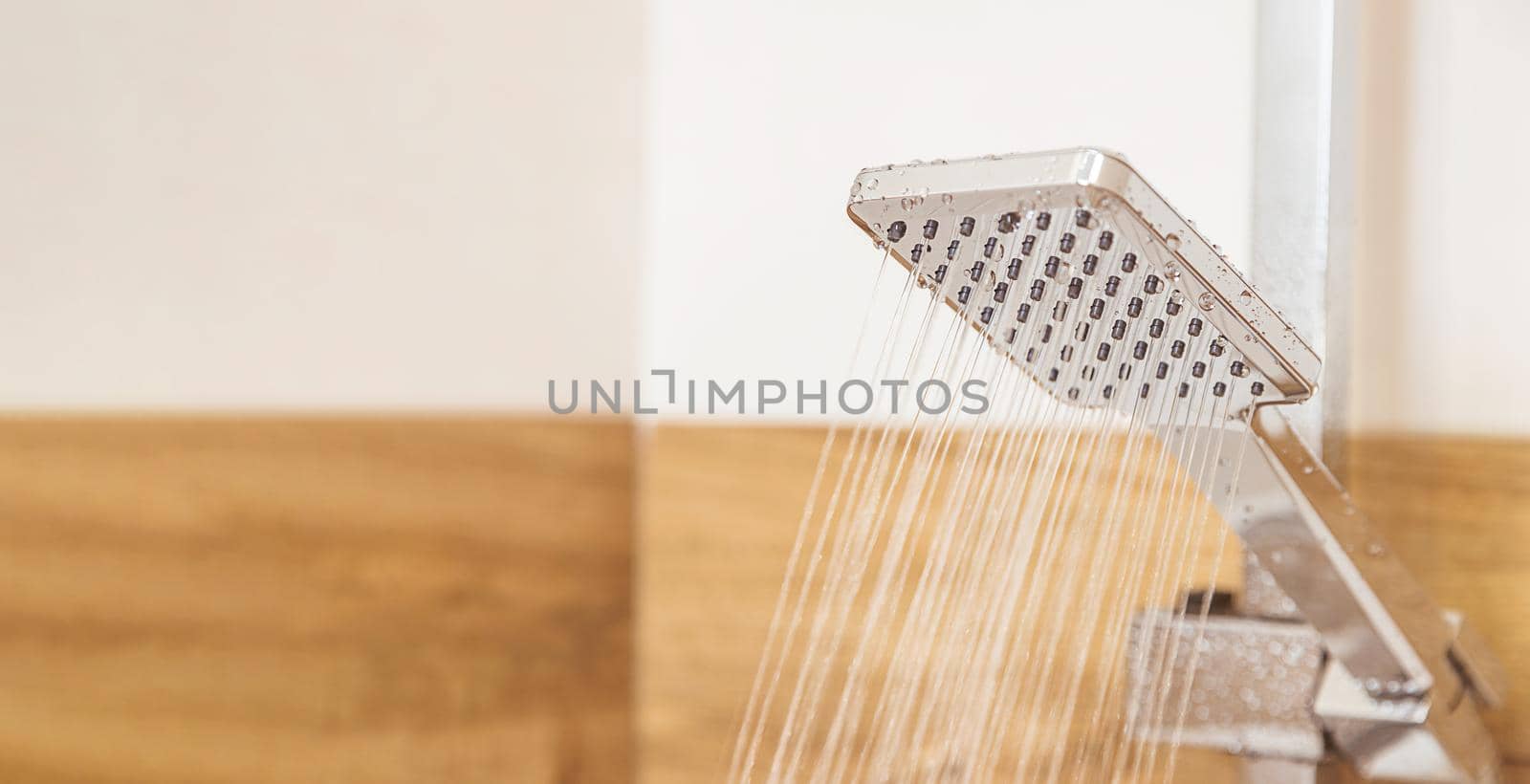 close-up, a chrome shower hangs on a ceramic wall in a shower cabin, water pours out of it. Copy space for text. Concept, water saving, reasonable consumption, plumbing equipment, personal hygiene