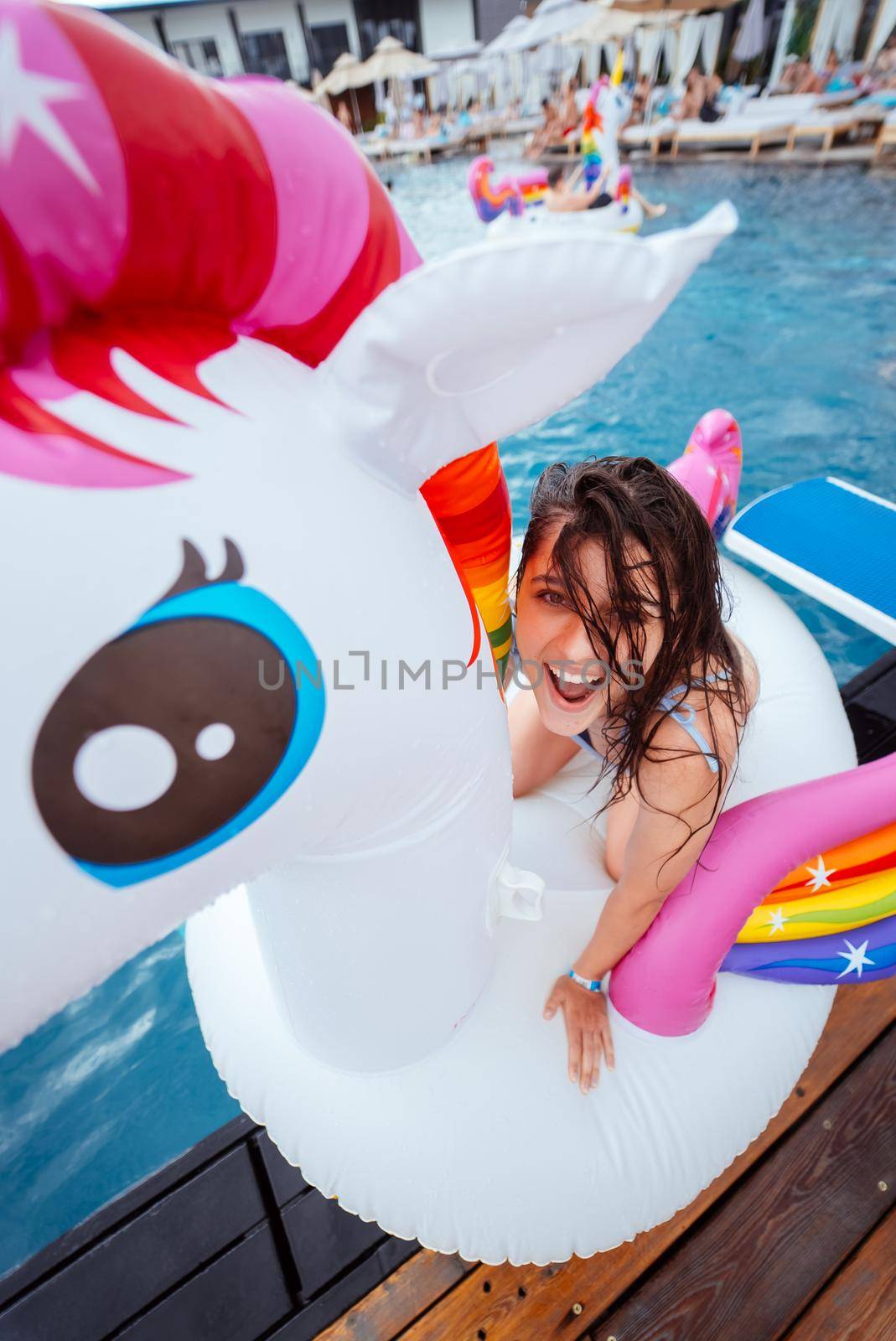 Happy young woman sitting on inflatable unicorn toy mattress by the pool. Girl relaxing sunbathing enjoying travel holidays at resort pool