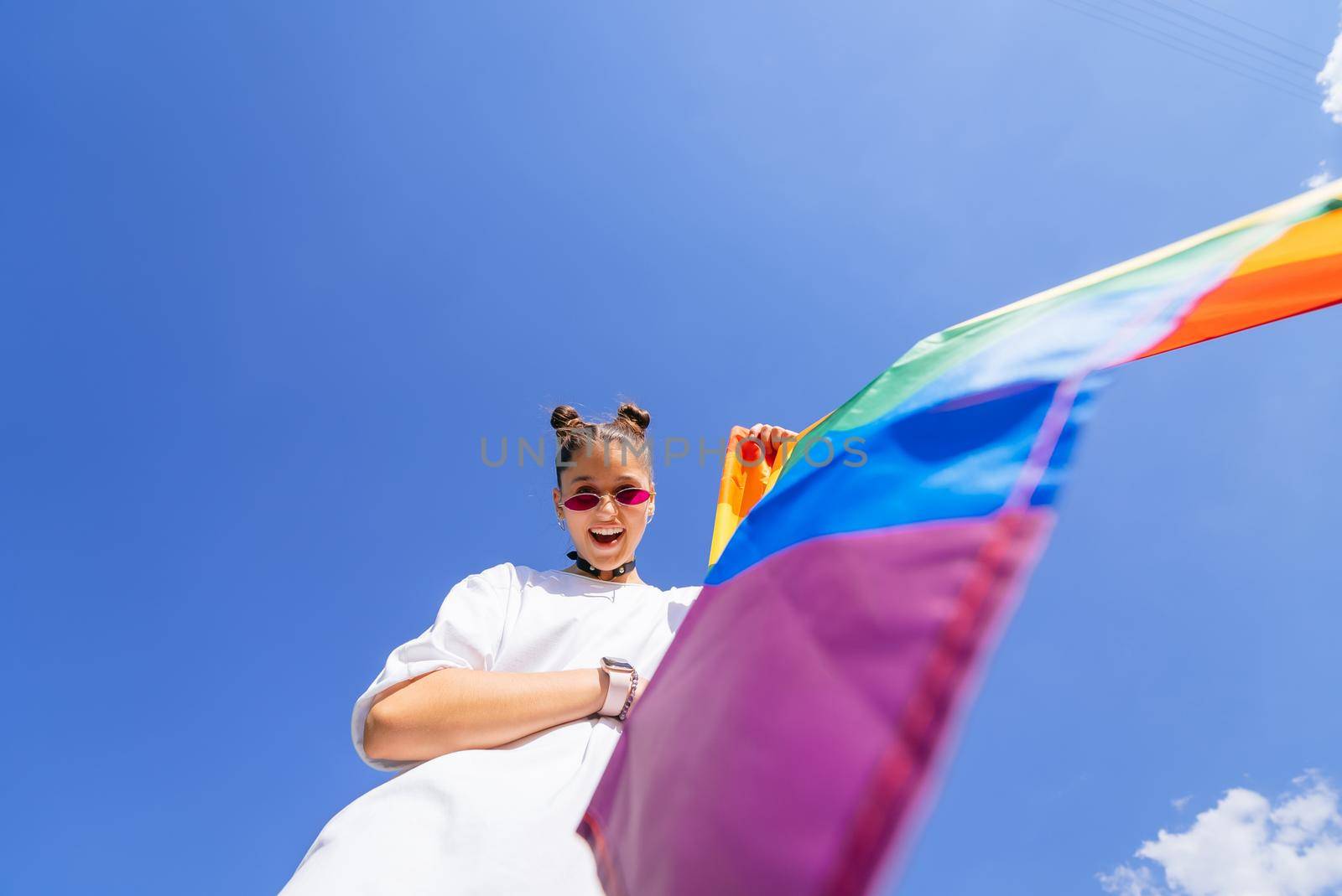 A young woman develops a rainbow flag against the sky in support of the LGBT community