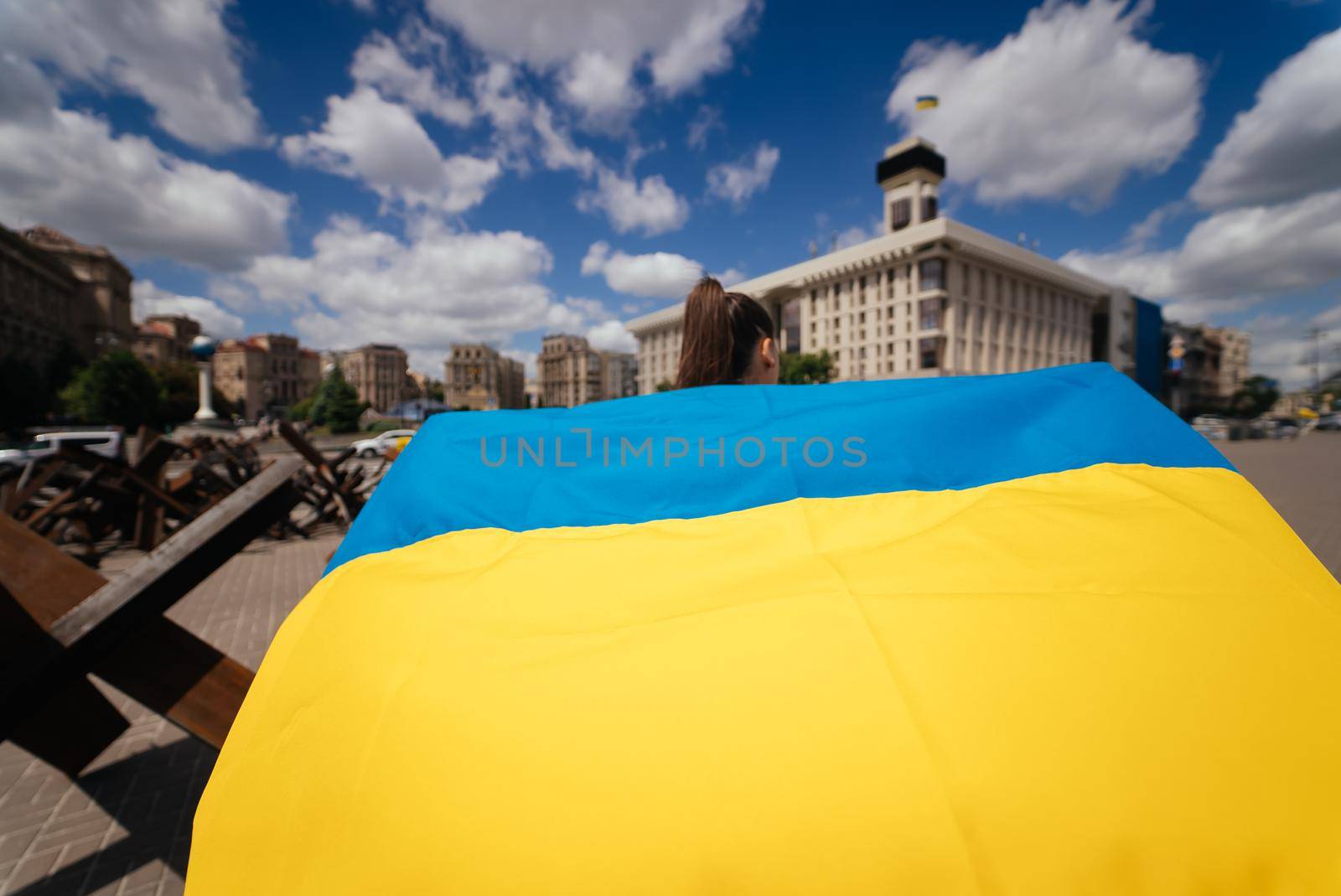 A young woman carries the flag of Ukraine fluttering behind her in the street