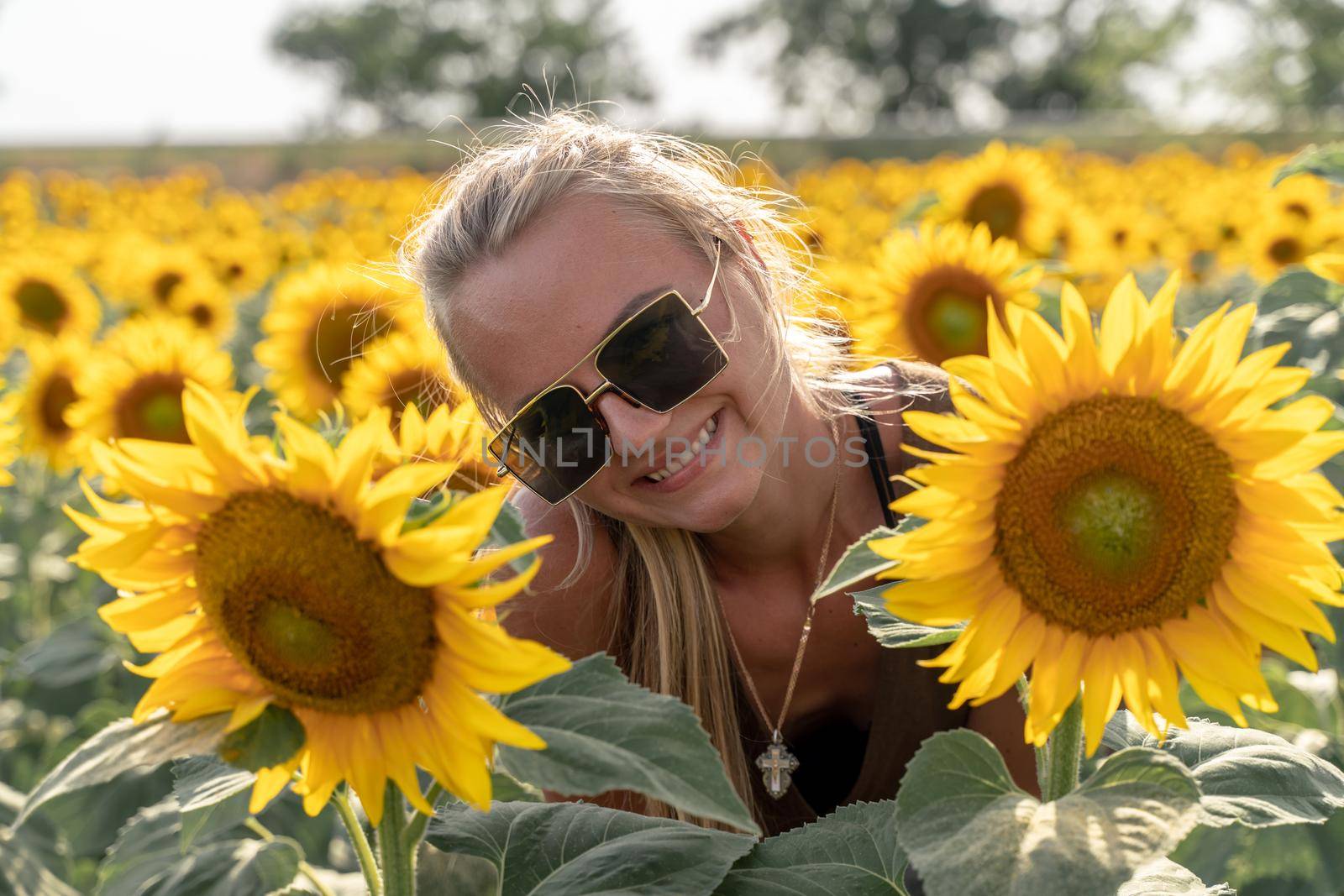 Beautiful woman in sunflower field at sunset enjoying summer nature. Attractive blonde with long healthy hair