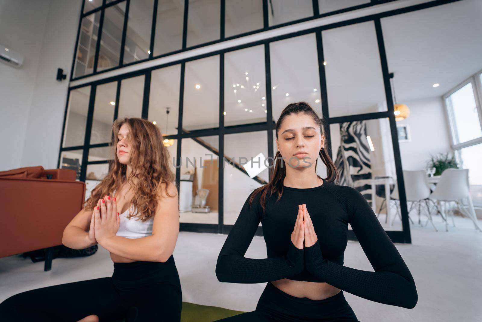 Two young women meditating in lotus pose with hands in namaste. Yoga