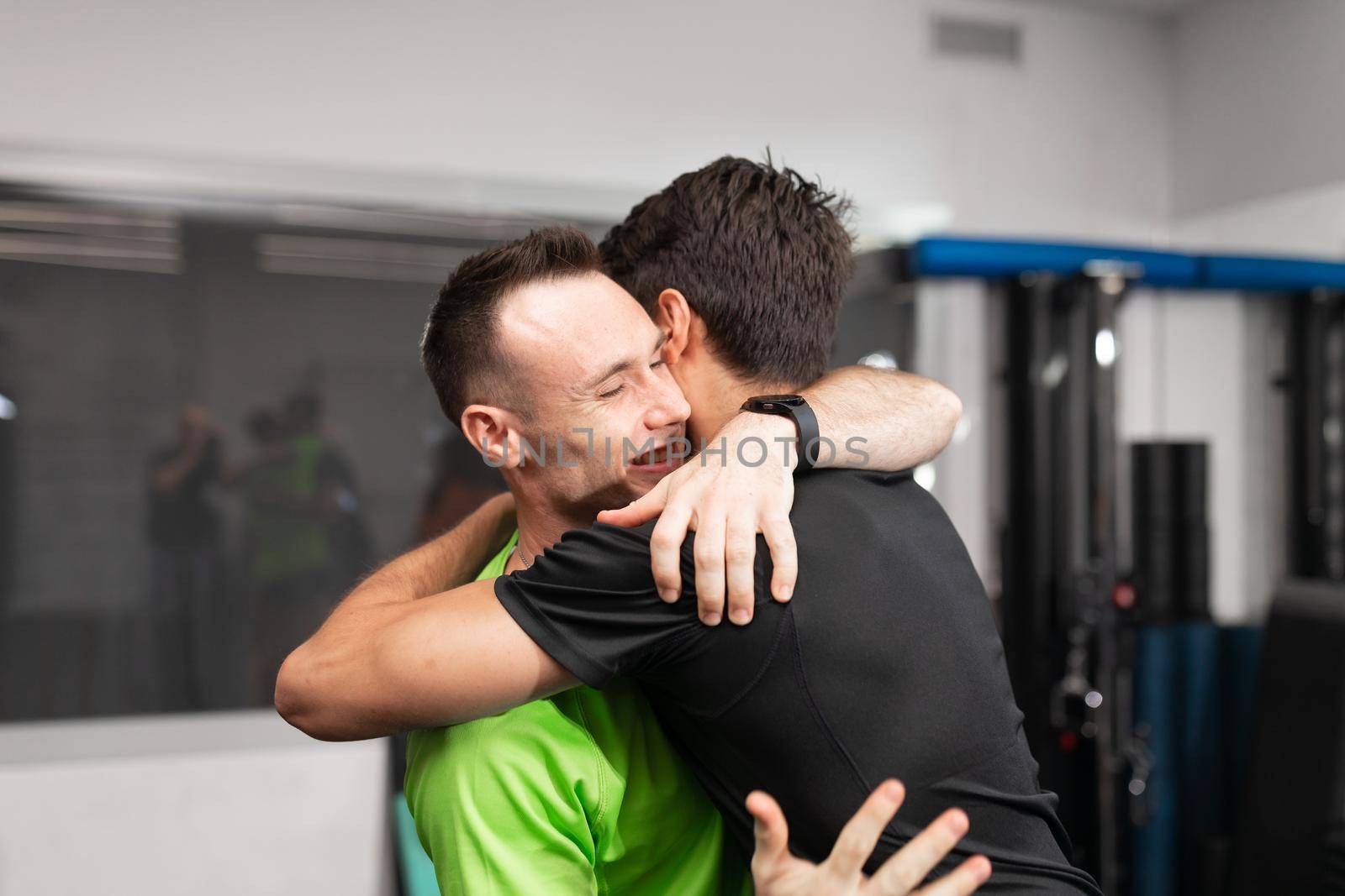 Close-up of a male trainee and trainer giving each other a hug at the gym by stockrojoverdeyazul