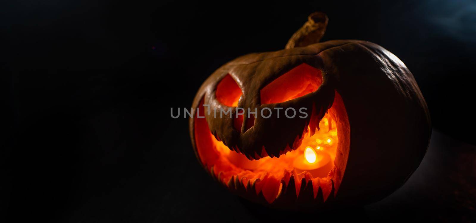A creepy pumpkin with a carved grimace glows. Jack on a lantern in the dark