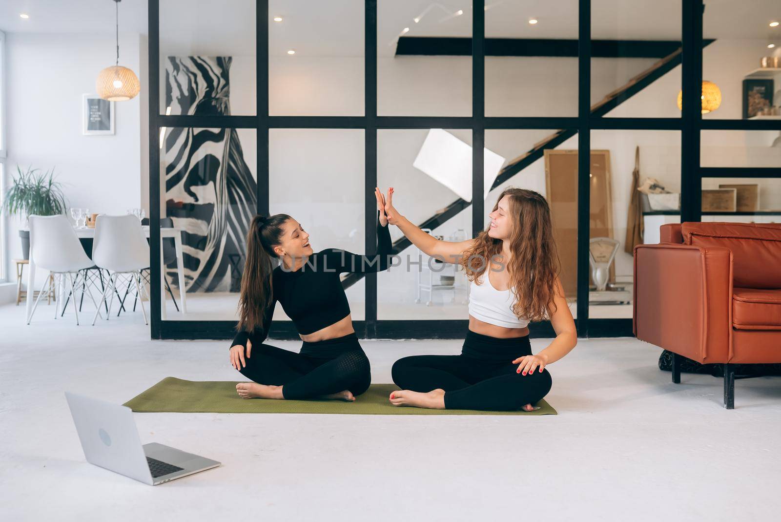 Two women while sitting in the lotus position give a high five by teksomolika