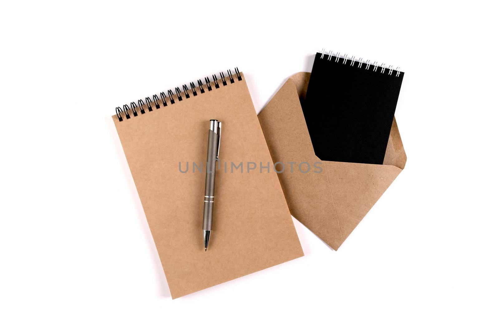 Blank spiral notepads and a recycled envelope stacked on a white background next to an automatic pen. Education, office, environmental protection, zero waste.