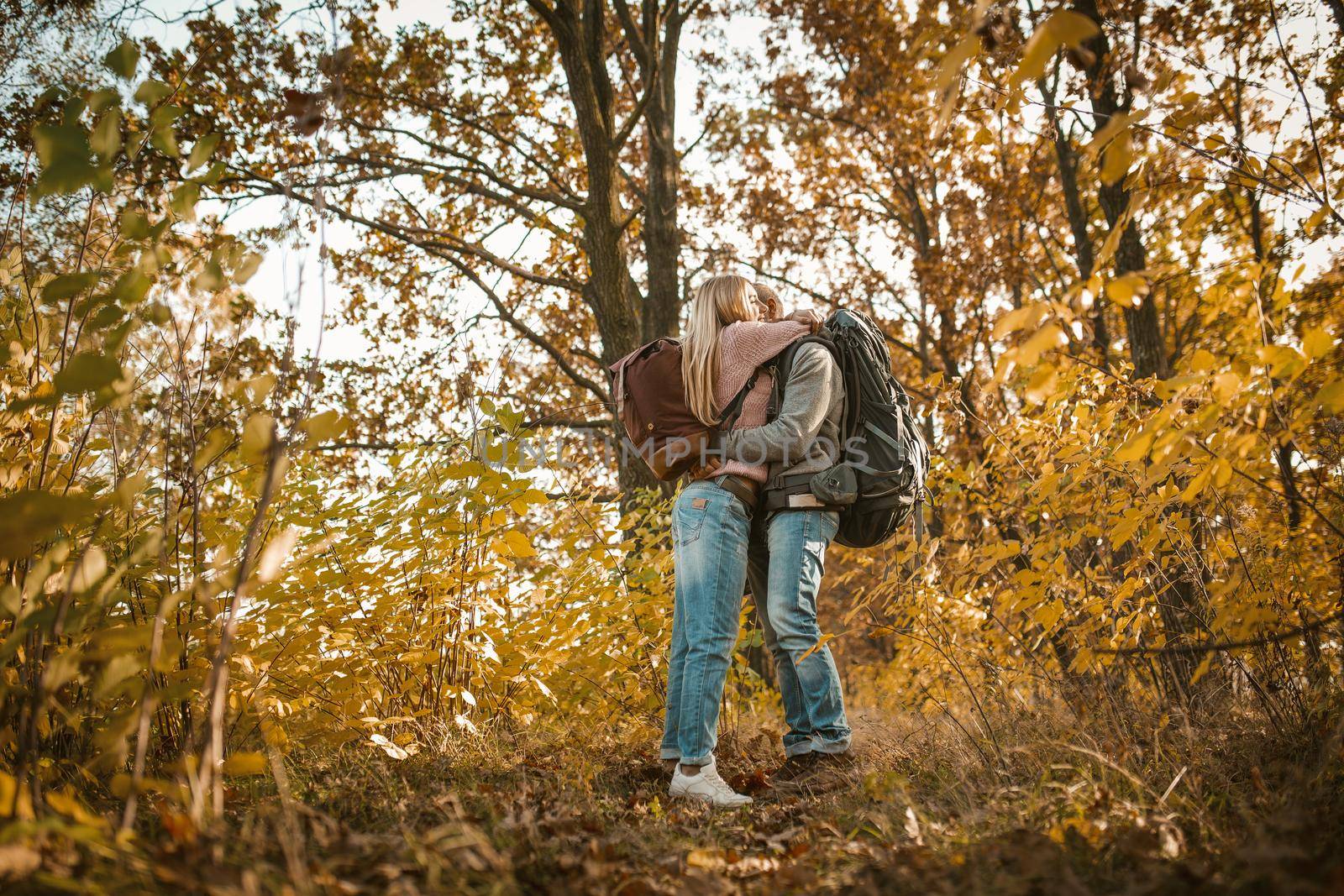 Loving couple of travelers hugs admiring the autumn nature. Young people stand embracing amid multicolor autumn nature. Shot from below. Love and hiking concept by LipikStockMedia