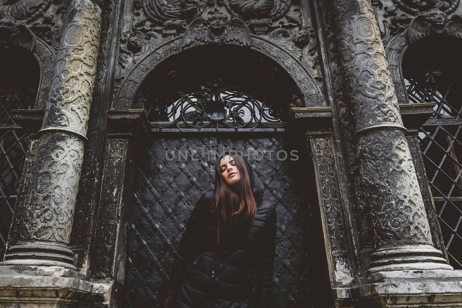 The young girl stands on the background of the old gothic wall.