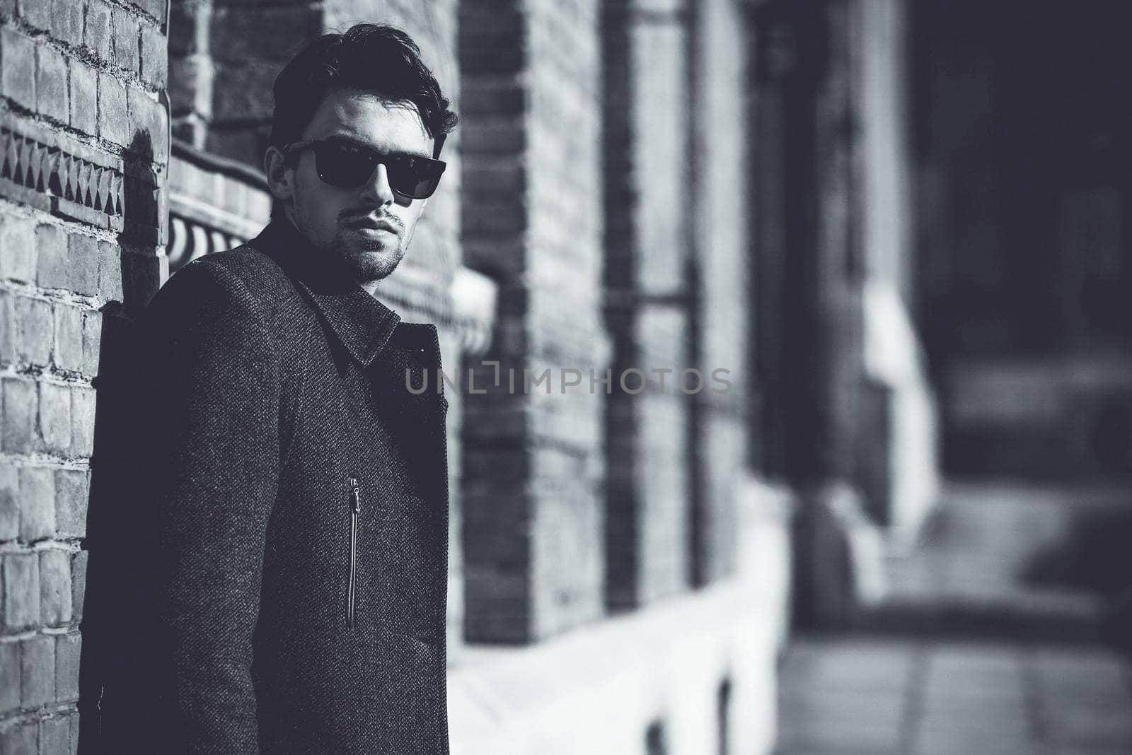 Portrait of fashionable well dressed man with beard posing outdoors looking away, confident and focused mature man in coat standing on a brick wall background, elegant fashion model.
