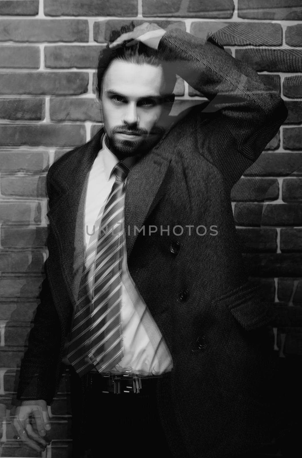 Portrait of fashionable well dressed man with beard posing outdoors looking away, confident and focused mature man in coat standing on a brick wall background, elegant fashion model.