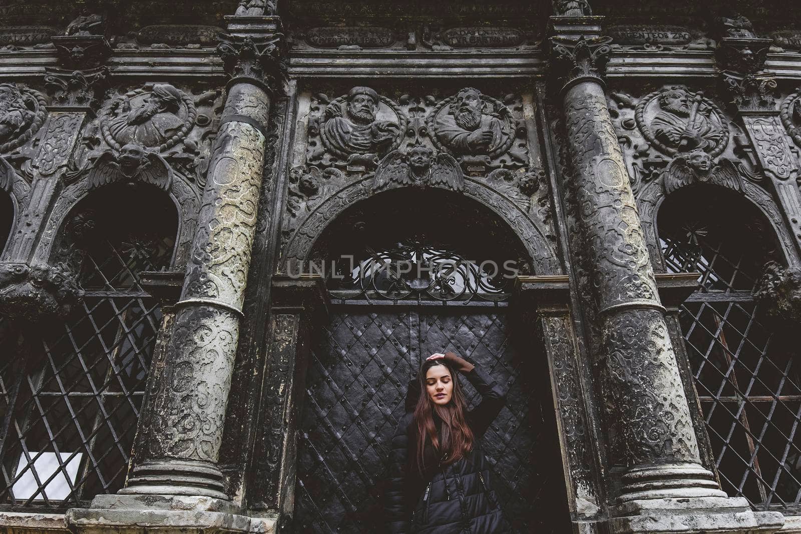 The young girl stands on the background of the old gothic wall.